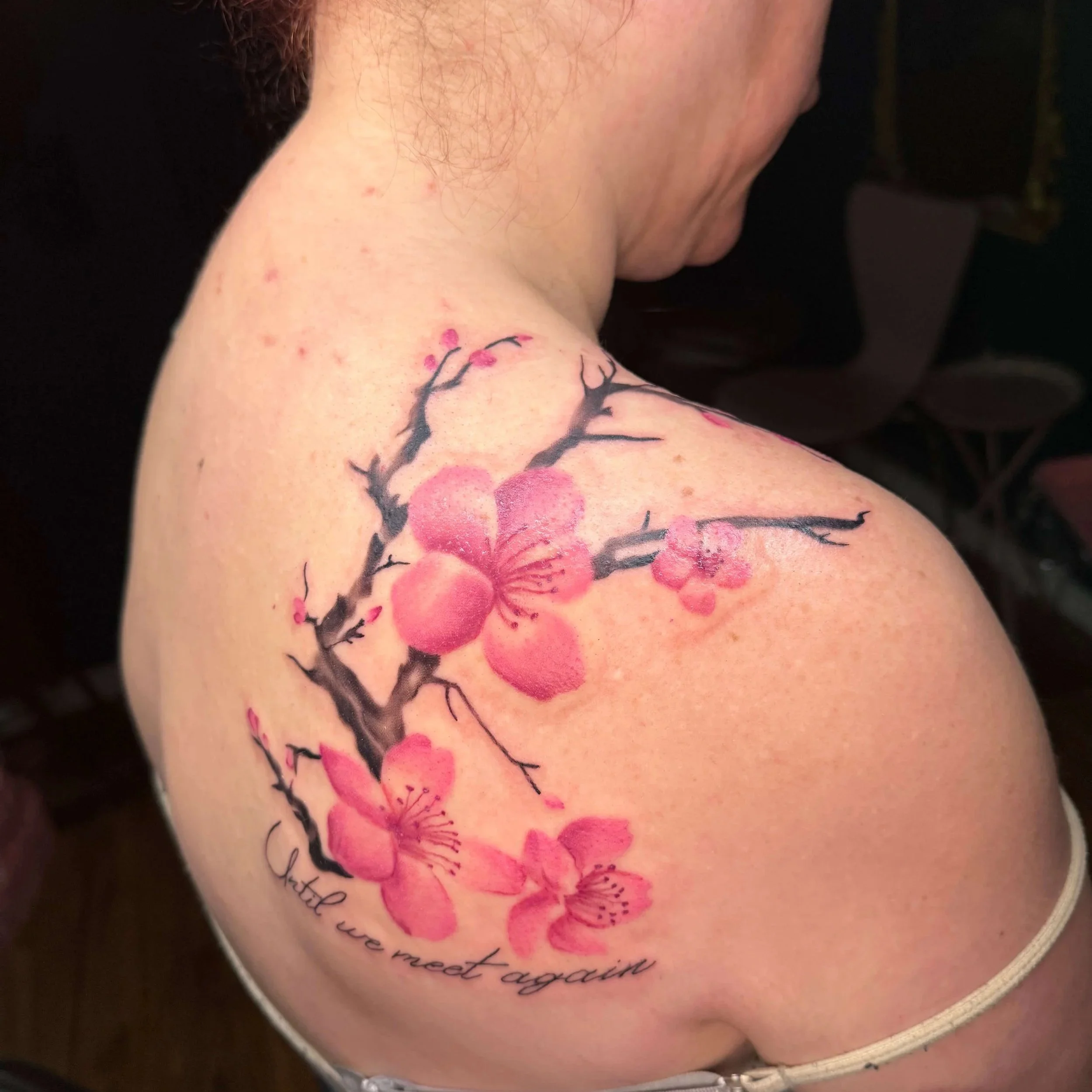 Watercolor and black and gray realistic tattoo of vibrant cherry blossoms and branches. This tattoo is on a back shoulder curving up and over to the clients chest. It was tattooed by Erin Peterson.