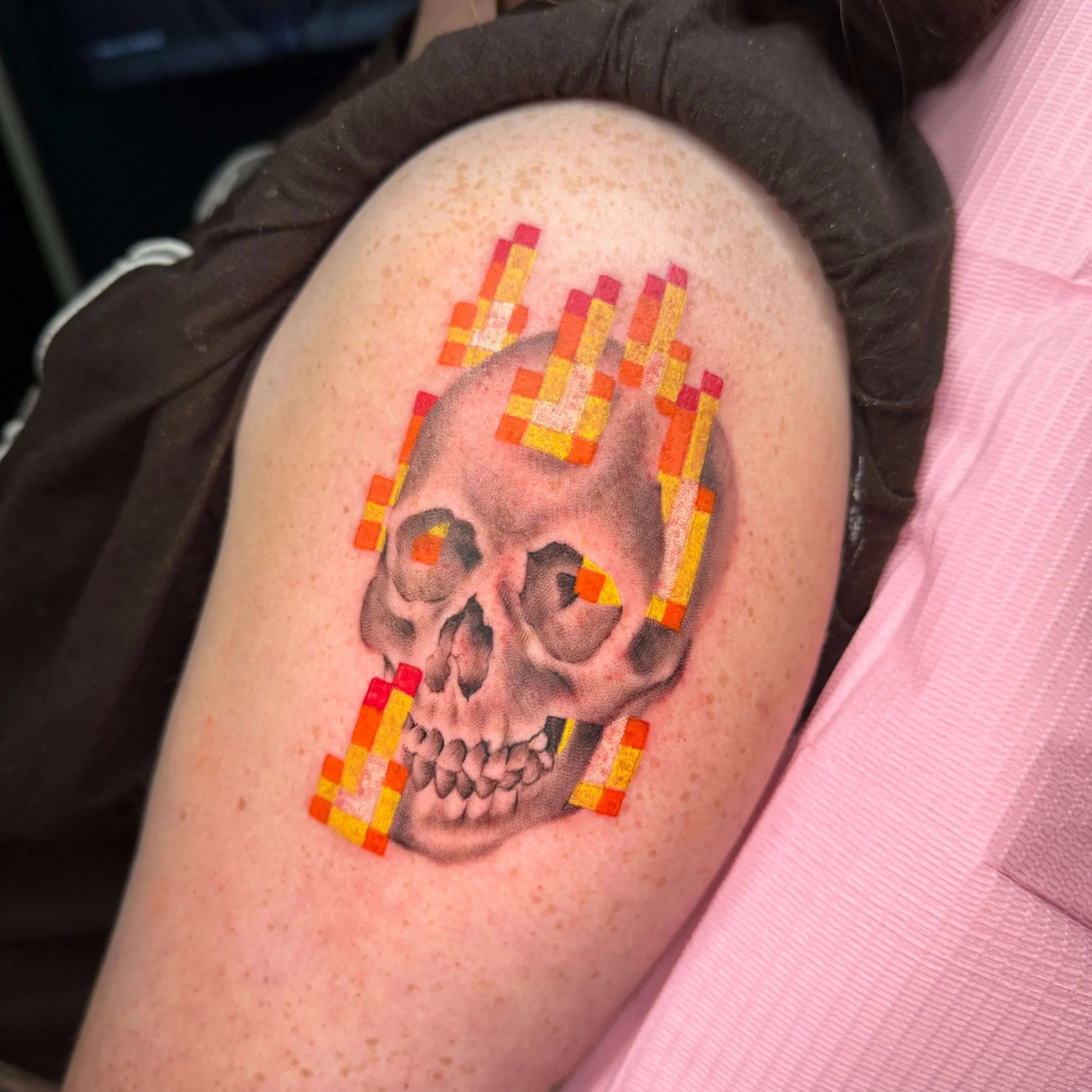 A black and gray realism skull tattoo with color 8 bit flames done as a tribute to a Minecraft painting. It was done by Erin Peterson in Denton Texas.