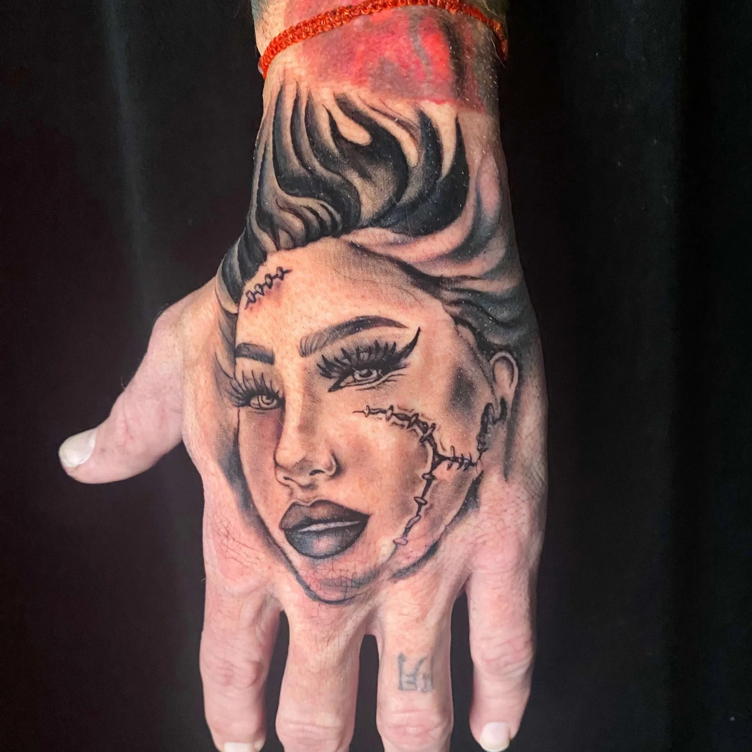 Black and gray realism hand tattoo inspired by the Bride of Frankenstein done by Erin Peterson. It features soft facial details, flowing hair up the clients wrist, and face stitching.
