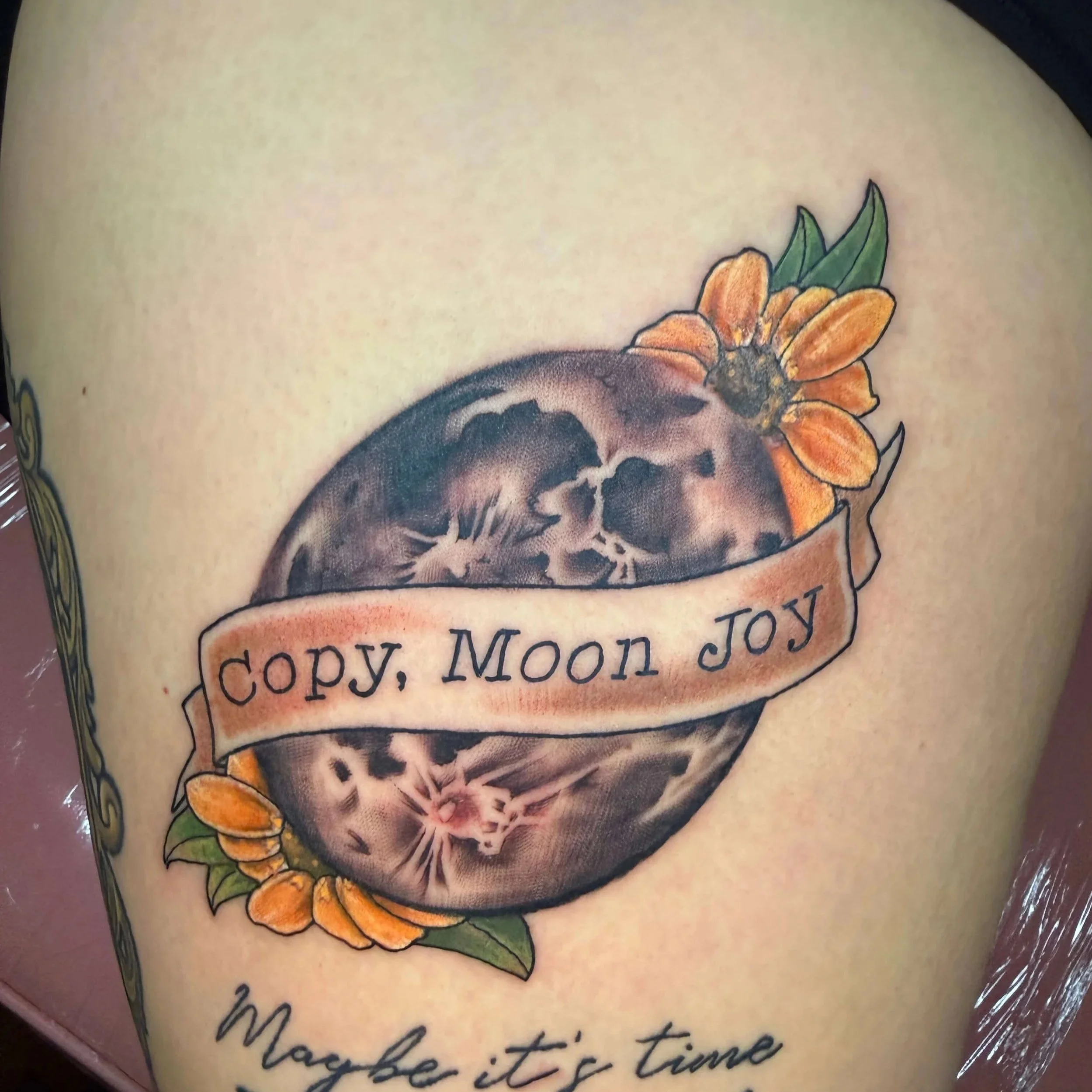 Full moon tattoo with flowers and banner reading Copy, Moon Joy by Erin Peterson at Integrity Tattoo in Denton Texas.