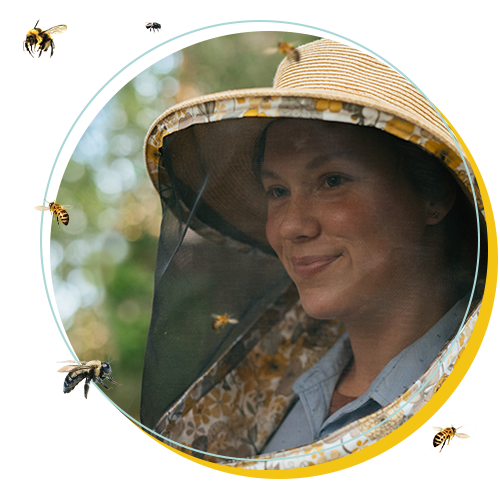 Portrait of The Peoples Bees' founder and director Christine Webster, wearing a beekeeping veil, surrounded by flying bees.