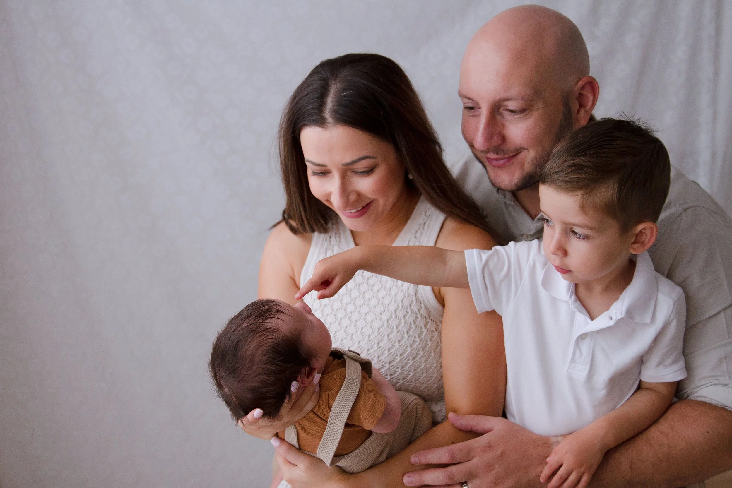toddler pointing to his newborn baby brothers nose. toddler interactions with newborn during family photos