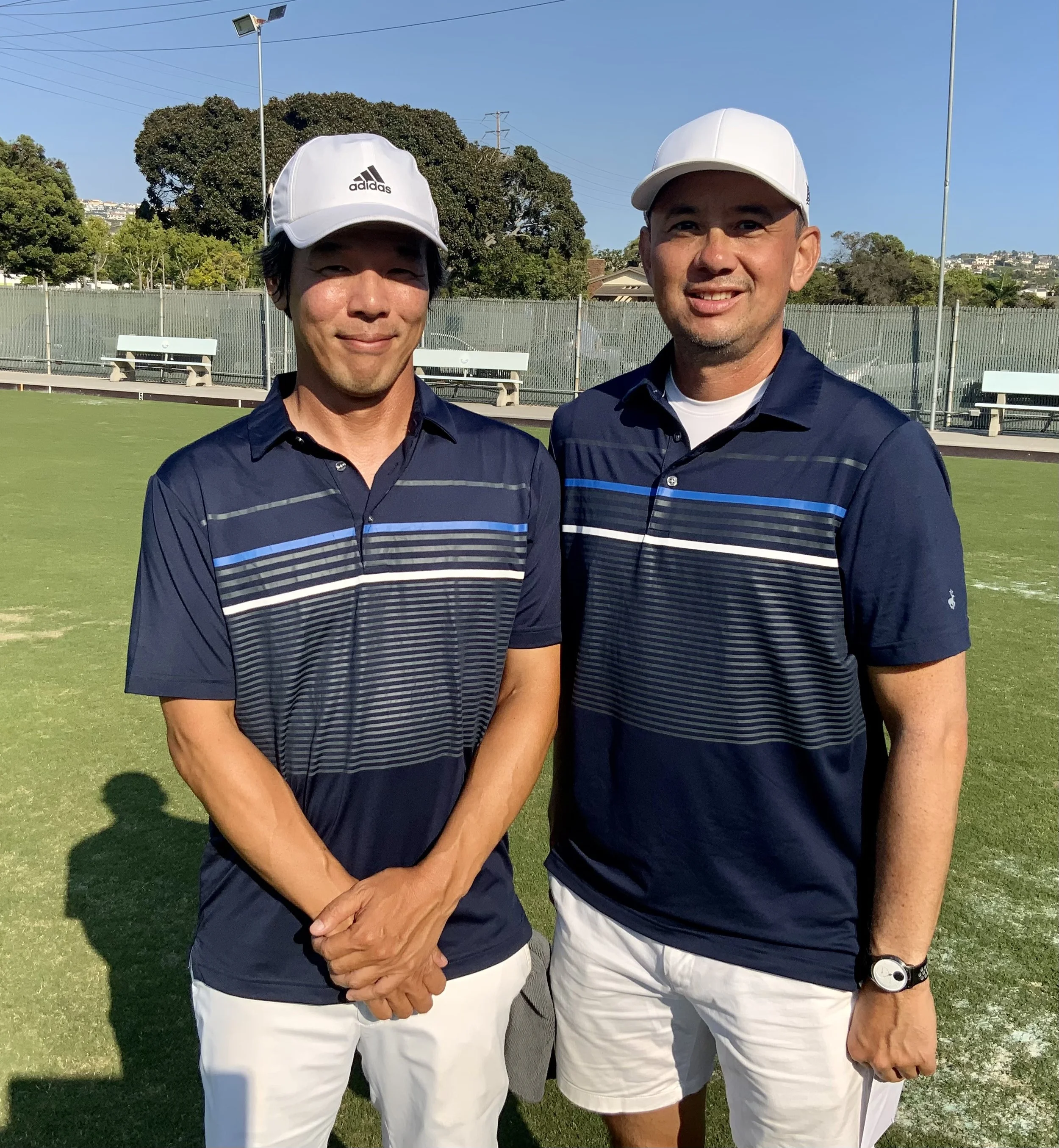 Two men in navy blue team shirts and white hats standing on a tennis court.