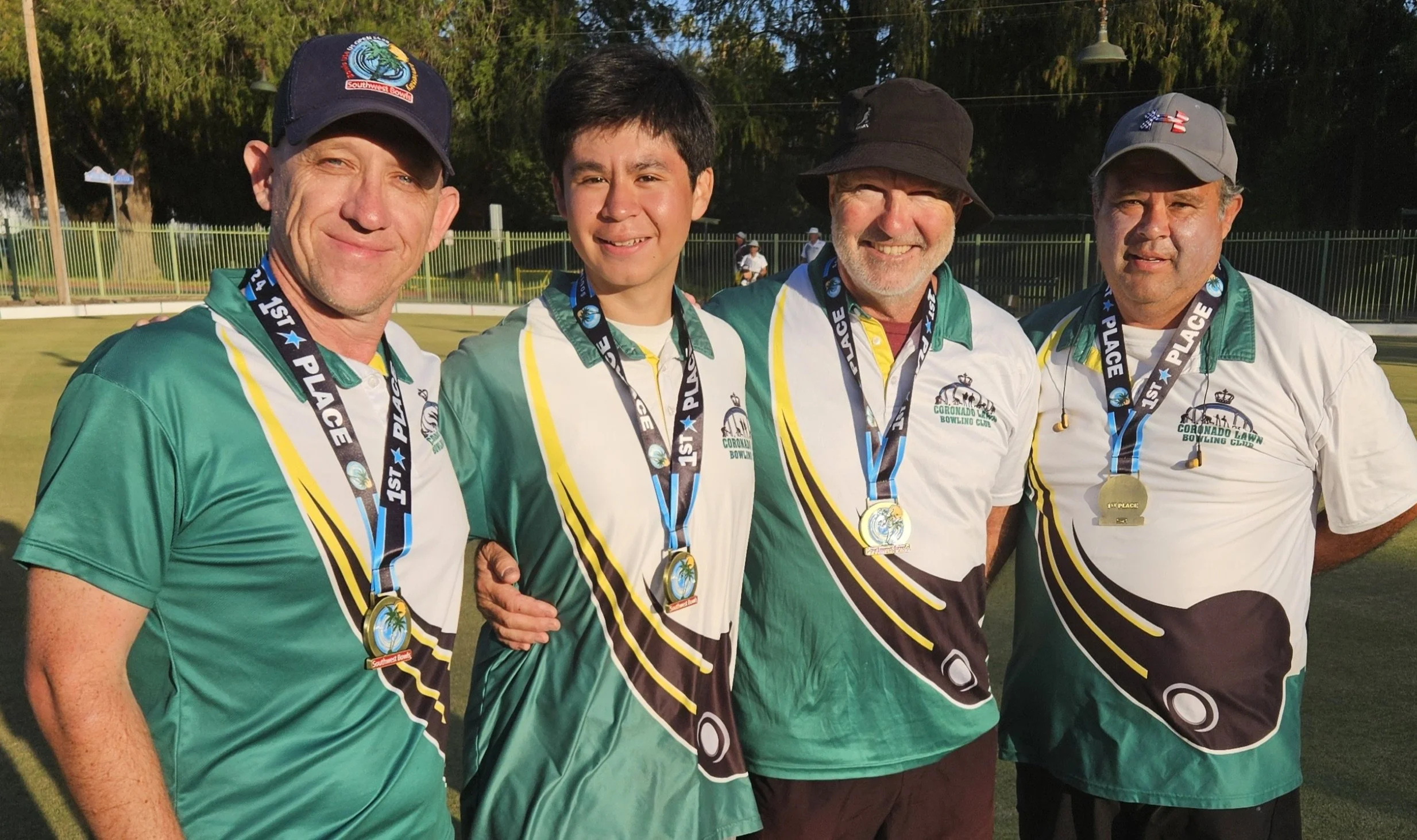 Four men standing together outdoors, wearing bowling jerseys and medals, celebrating their first-place win at a bowling tournament.