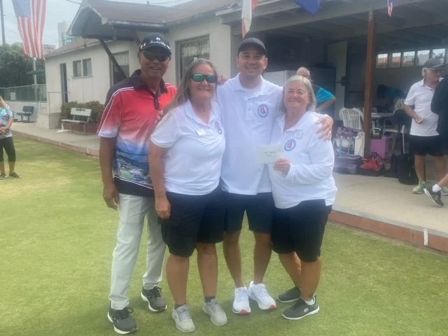 Four people, three women and one man, standing on a golf course, smiling and posing for a photo. They are dressed in casual sportswear, with some wearing sunglasses, and appear to be celebrating or participating in a golf event.