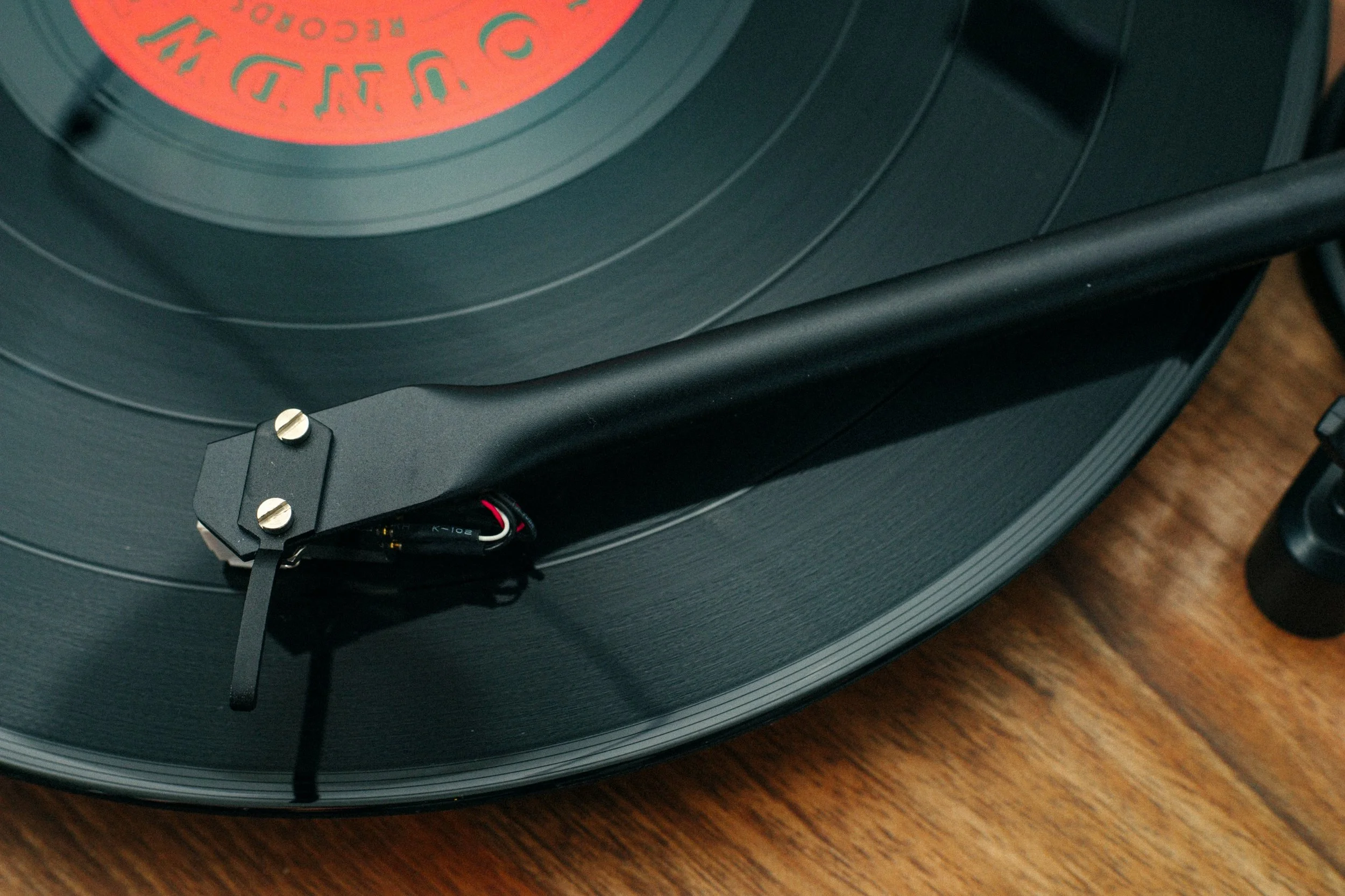 Close-up of a vintage-style black turntable with a black tonearm and stylus, sitting on a wooden surface.
