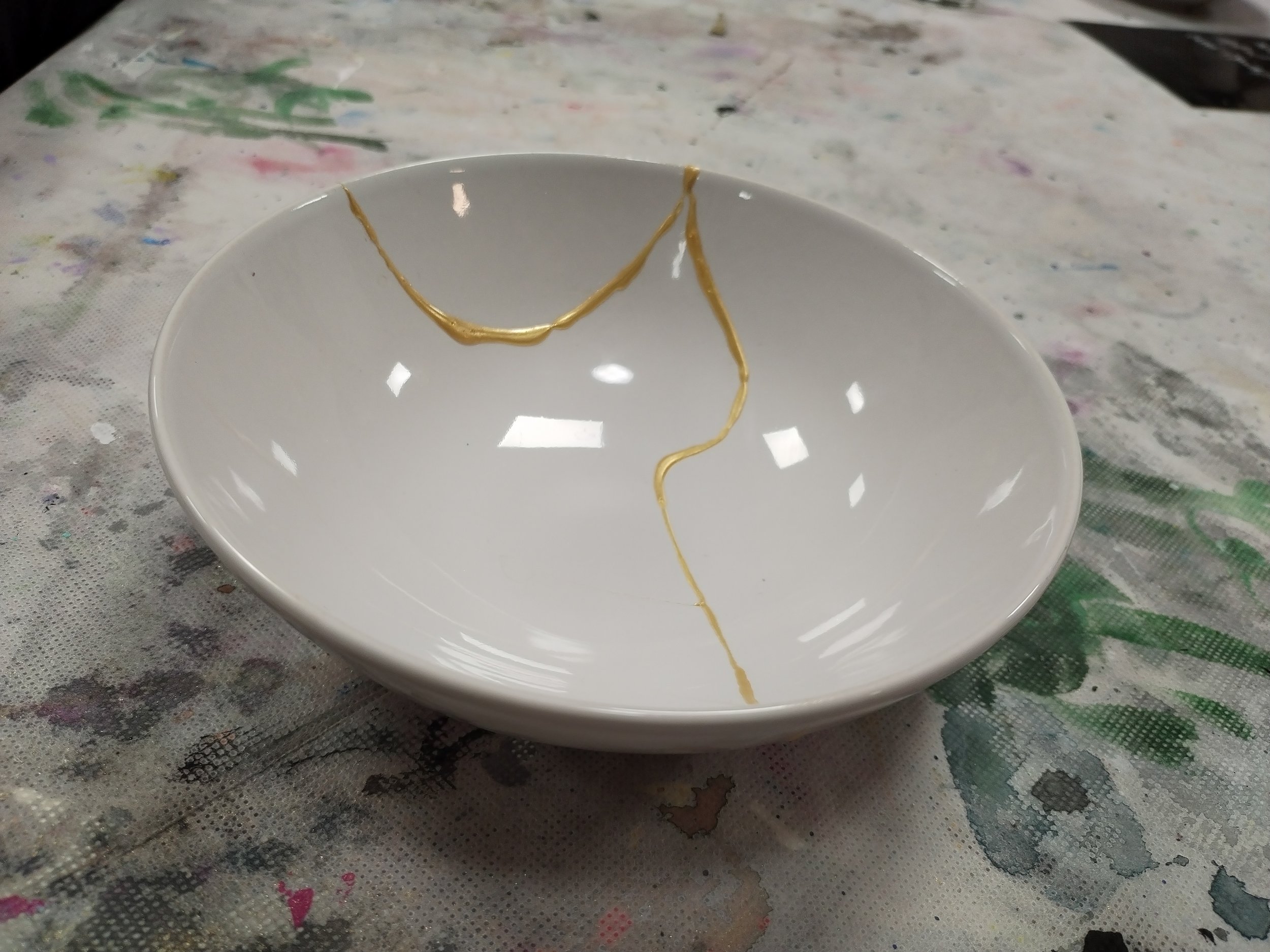 Mit Kintsugitechnik reparierte weiße Porzellanschale mit goldenen Nahtstellen, auf einem Arbeitstisch