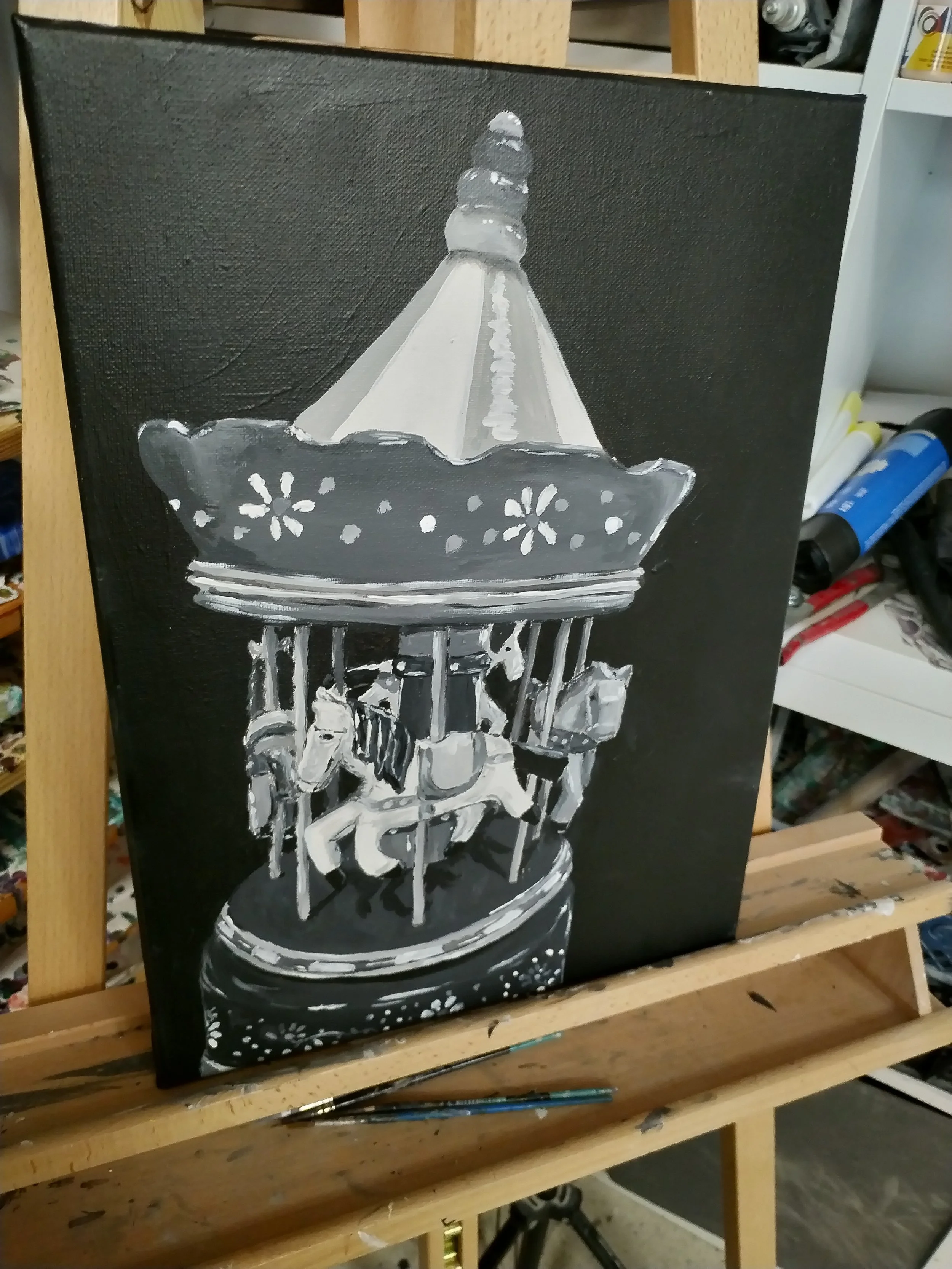 Reduzierte Schwarz-Weiß-Malerei eines nostalgischen Karussells mit Pferden auf dunklem Hintergrund. Das Objekt steht ruhig und zentral im Bild.