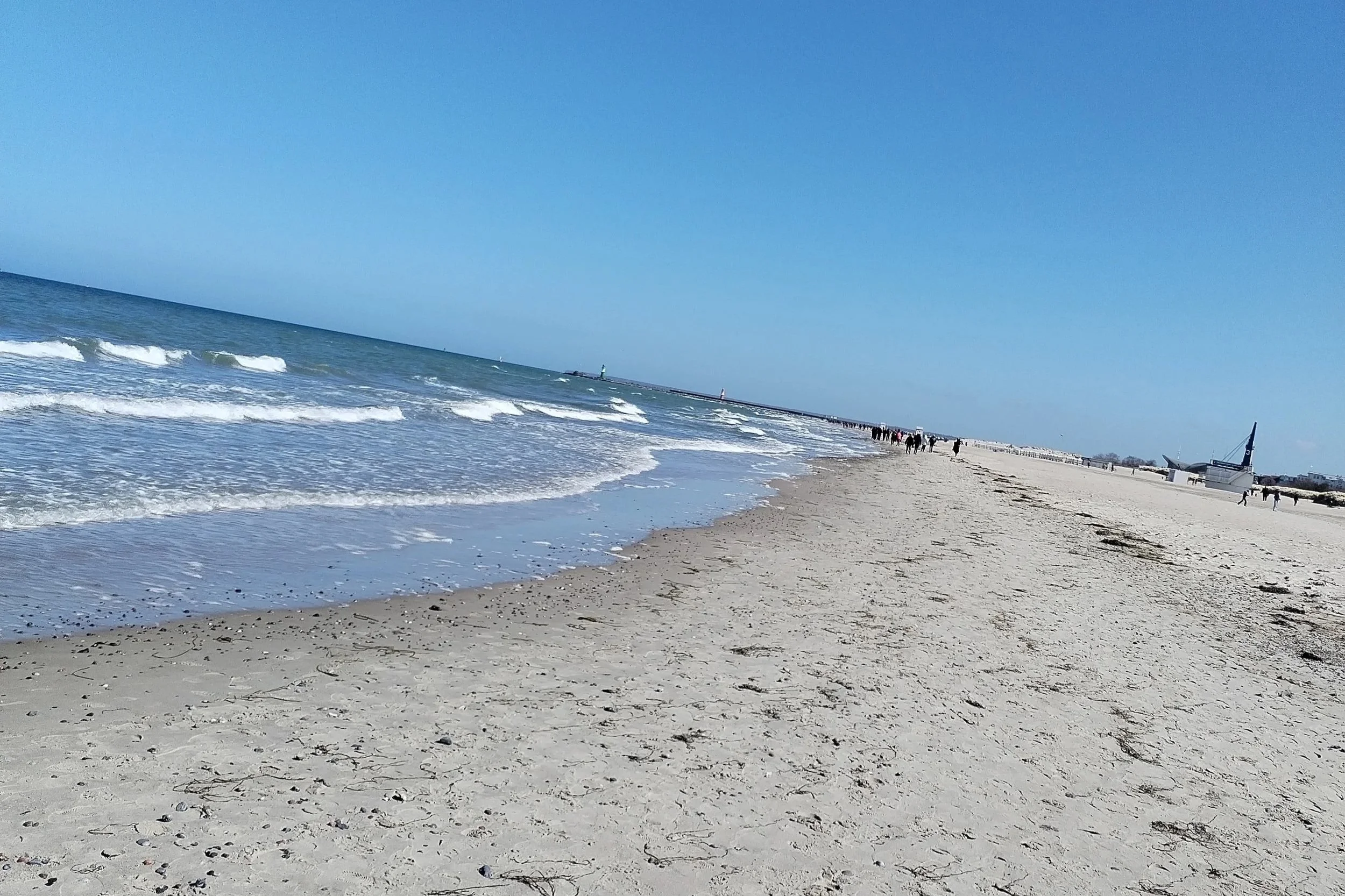 Strand von Warnemünde mit Wellengang und touristen im Hintergrund, bei schönstem Sonnenschein