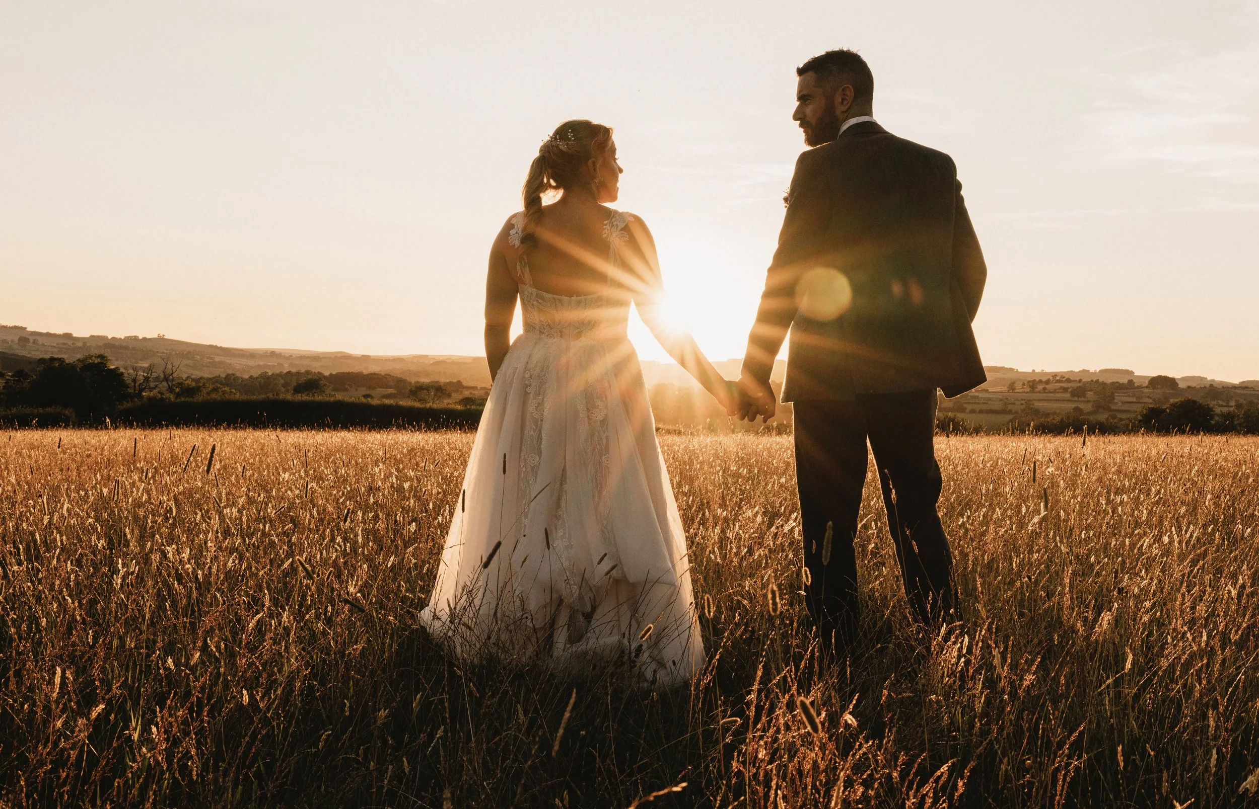 A bride and groom holding hands in a field at sunset.