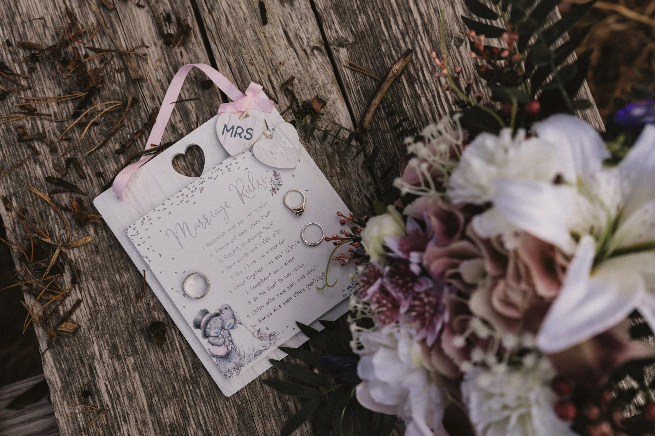 Wedding rings placed on a wedding advice card next to a bouquet of flowers on a rustic wooden surface.