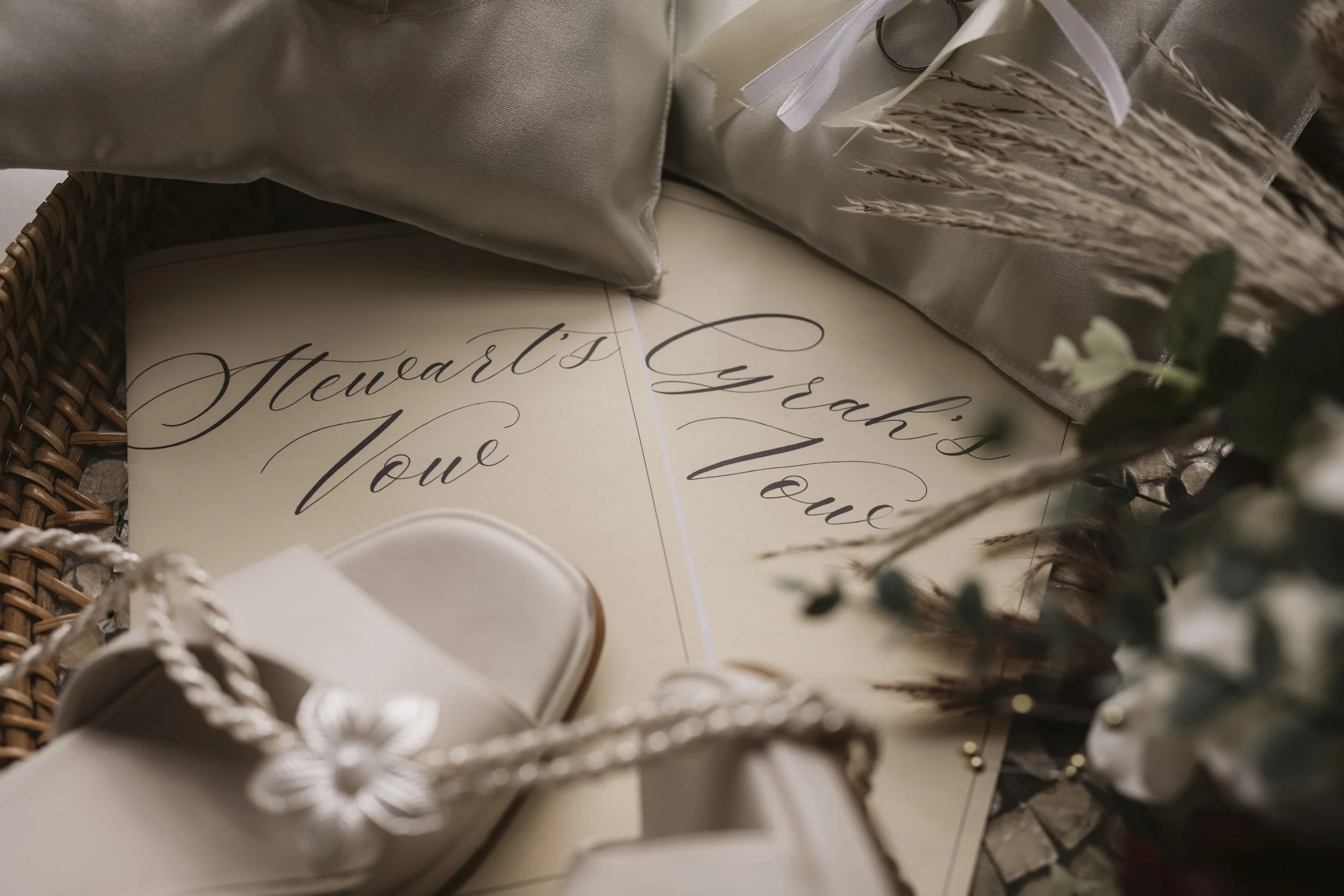 A wedding card with elegant cursive writing that says 'Thank you, Love.' It is surrounded by wedding shoes, a satin pillow, and floral decorations.