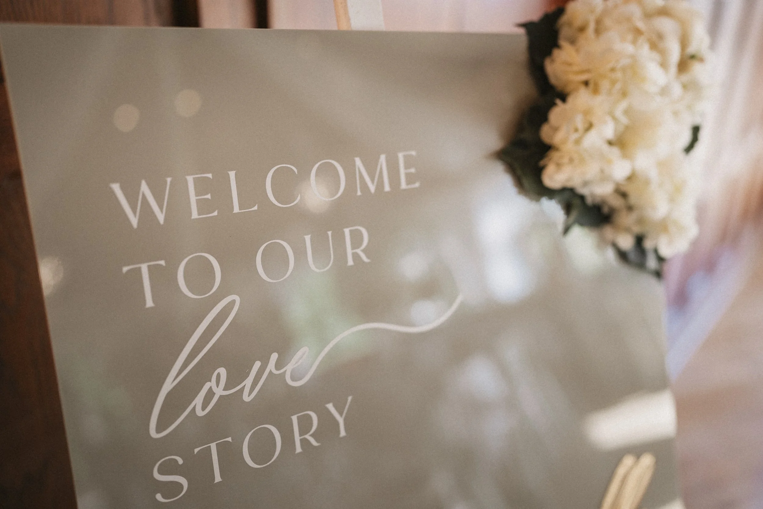 Mirror with the text 'Welcome to our love story' and white flowers attached to the top right corner.