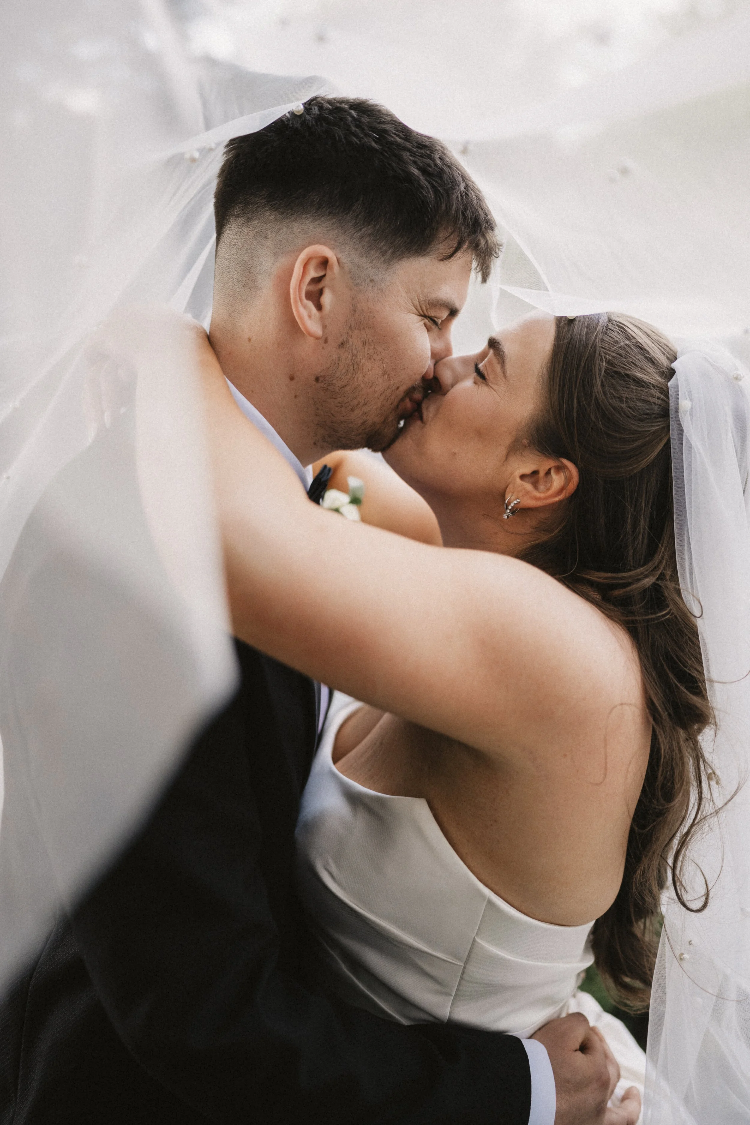 A bride and groom sharing a kiss under a wedding veil.
