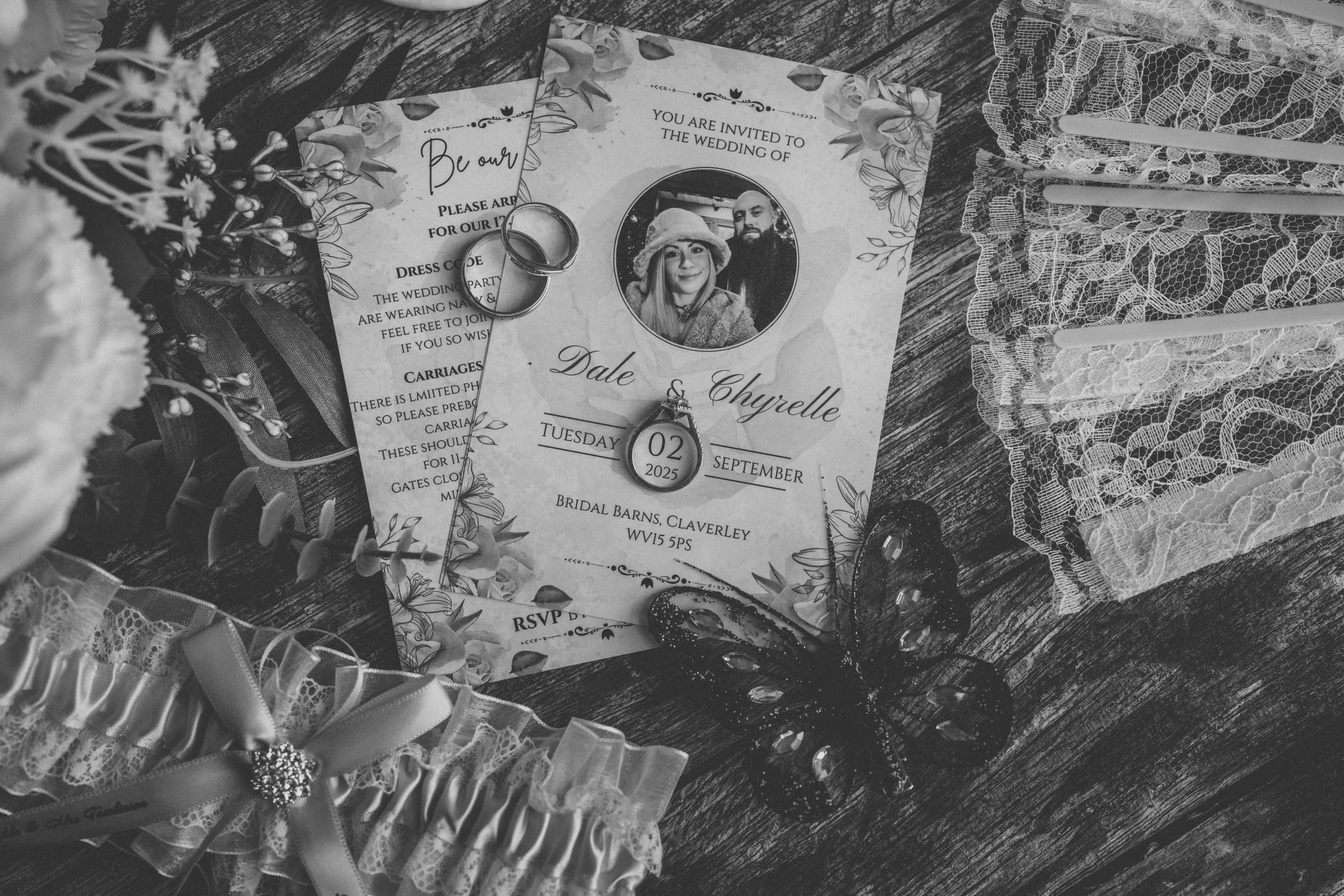 Wedding invitation with rings, a necklace, a butterfly hair clip, lace fabric, and decorative details placed on a wooden surface.