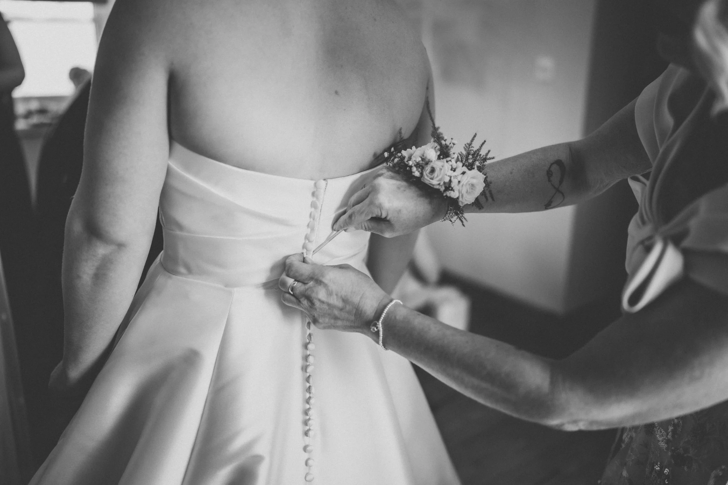 A person in a wedding dress being buttoned up by another person, possibly a bride getting ready for her wedding.
