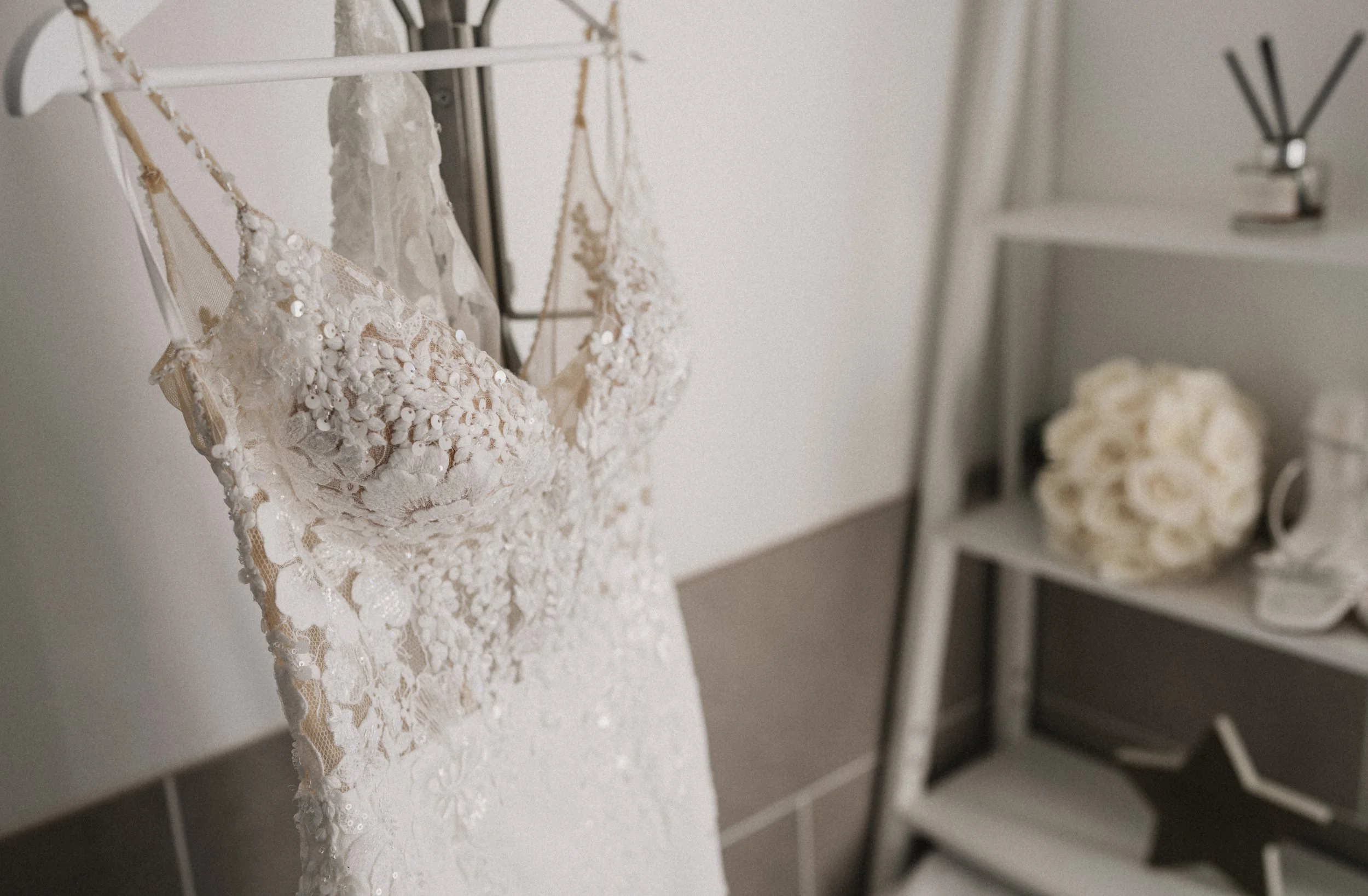 A white lace wedding dress with floral embroidery hanging on a white rack.
