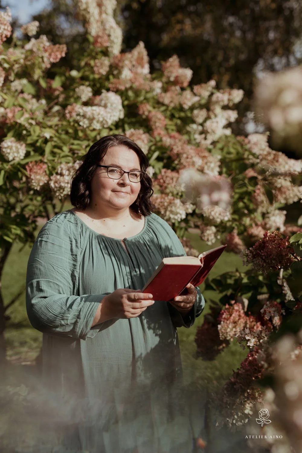 Annamari Typpö reads a book in the garden, with a flowering bush in the background.