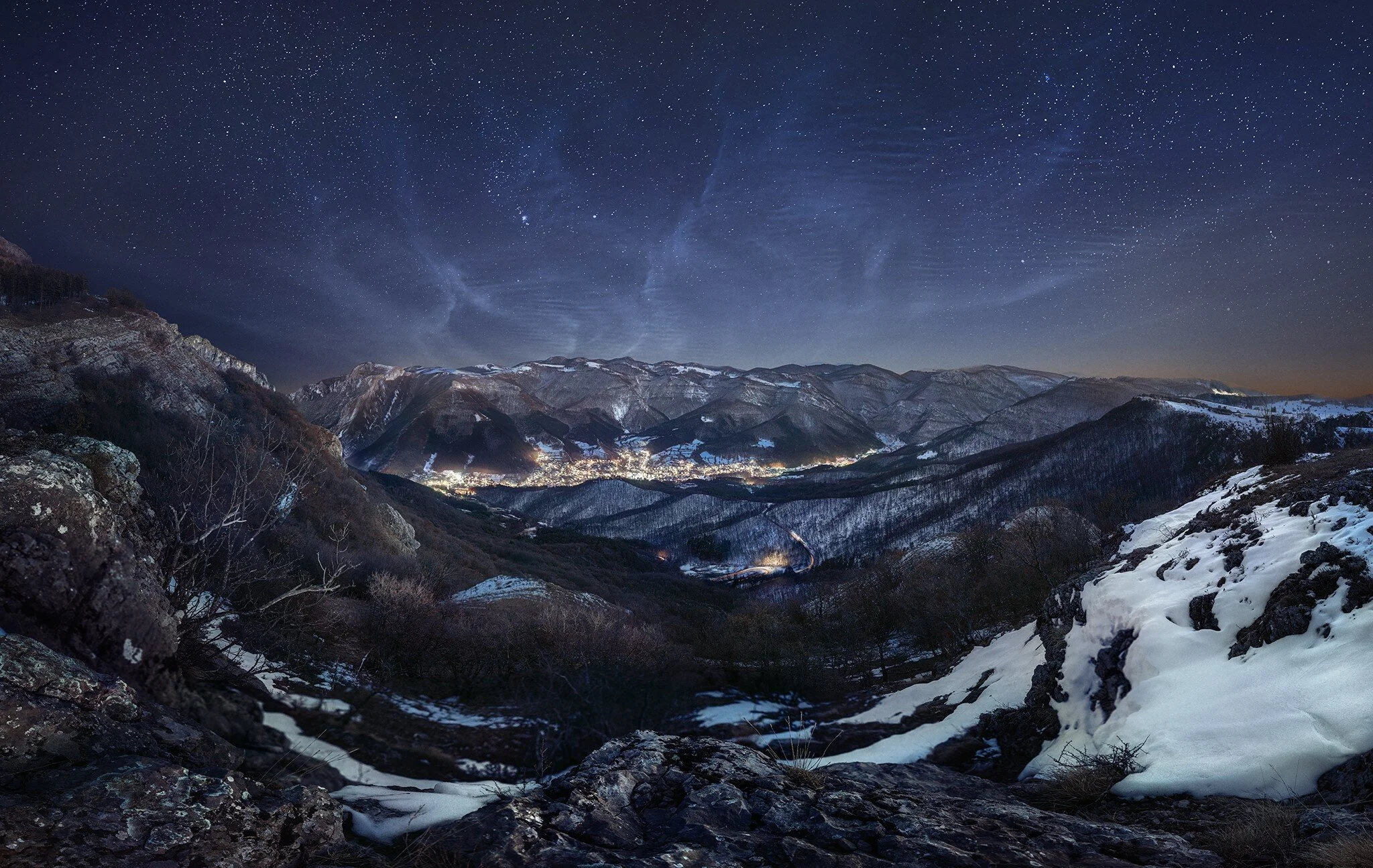 Nighttime mountain landscape with snow-covered slopes, valleys, and a star-filled sky.