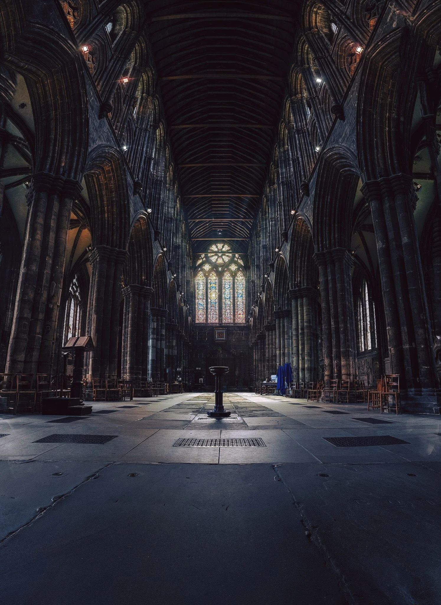 Interior view of a Gothic cathedral with high vaulted ceilings, large stained glass windows, and stone columns along the sides.