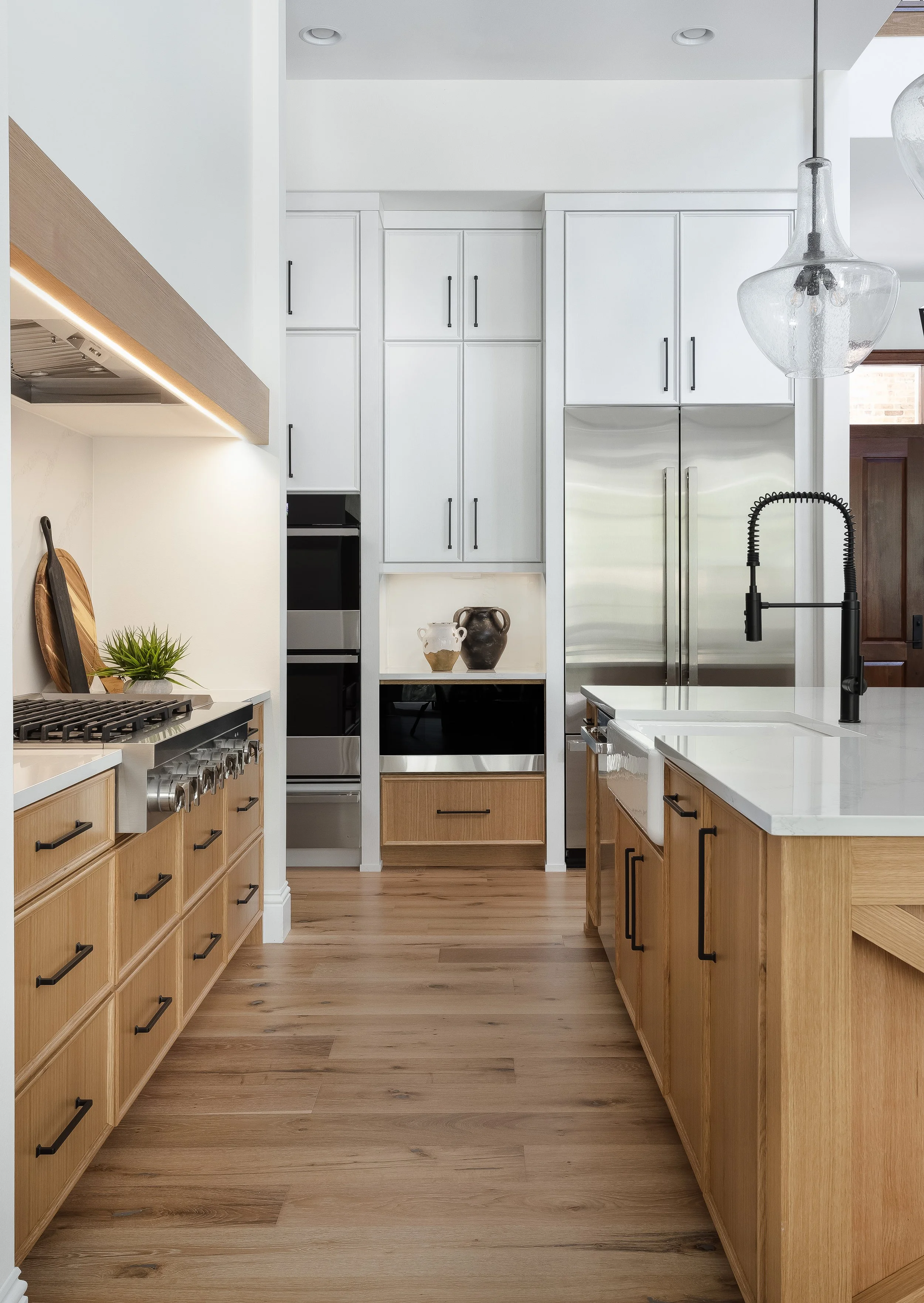 Modern kitchen with wooden cabinets, stainless steel appliances, white countertops, and a black faucet.