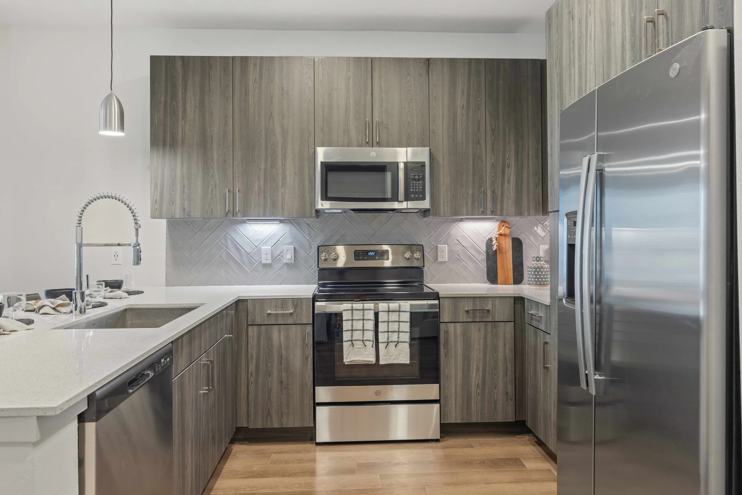 Modern kitchen with gray wooden cabinets, stainless steel appliances, and a white countertop with a sink.