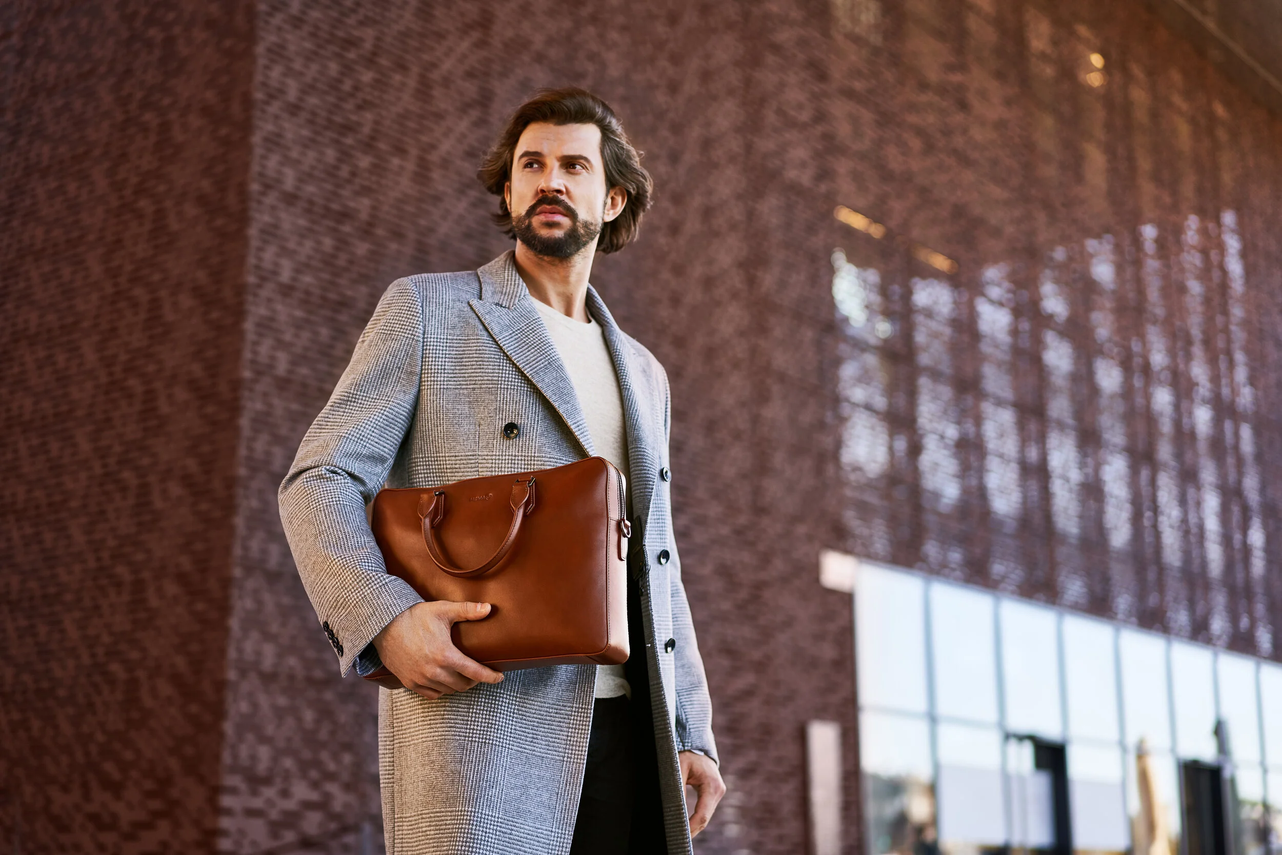 Mężczyzna z aktówką na tle brązowego budynku.