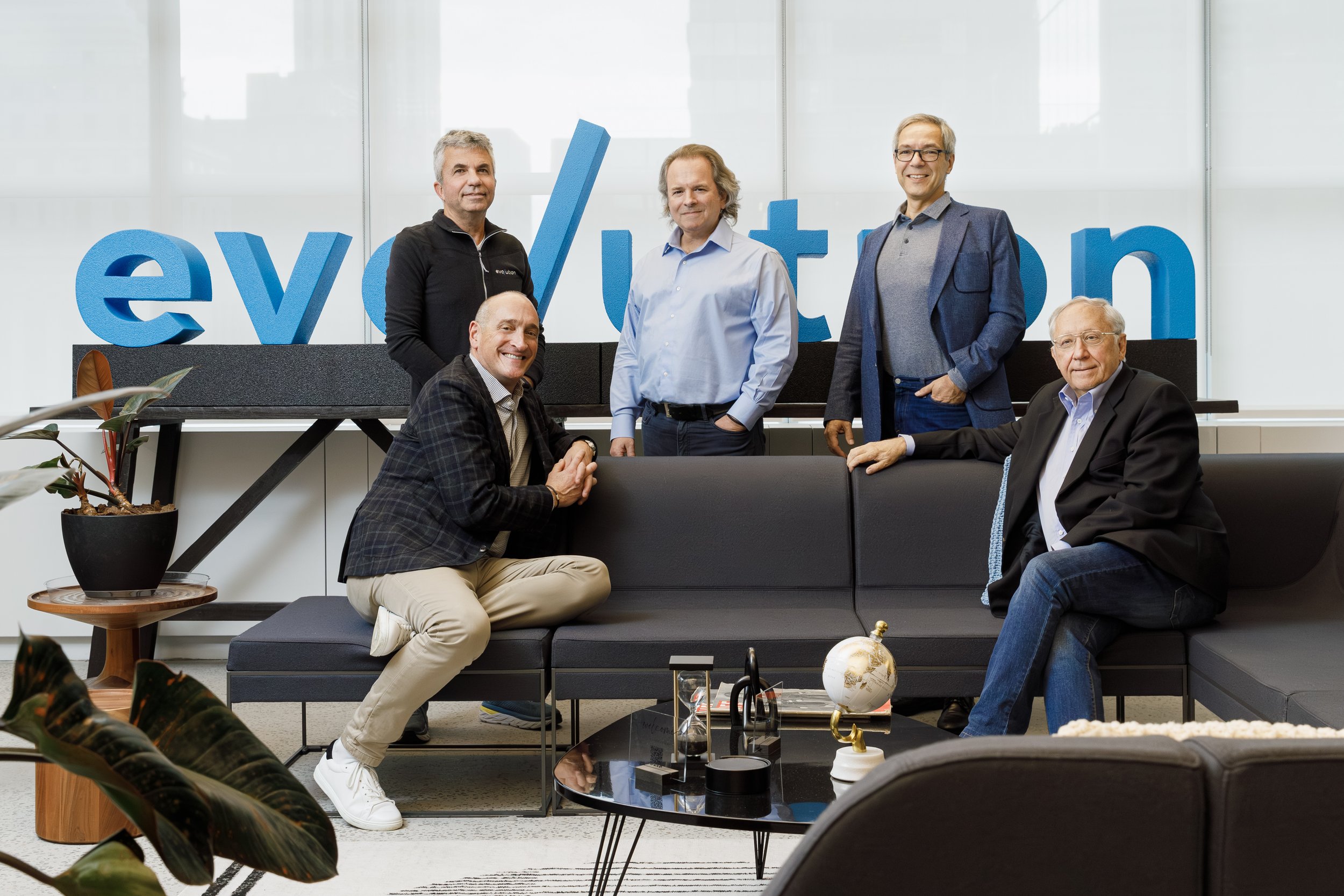 Five men in business attire gathered in a modern office, with a large sign reading 'evolution' behind them, posing for a group photo.