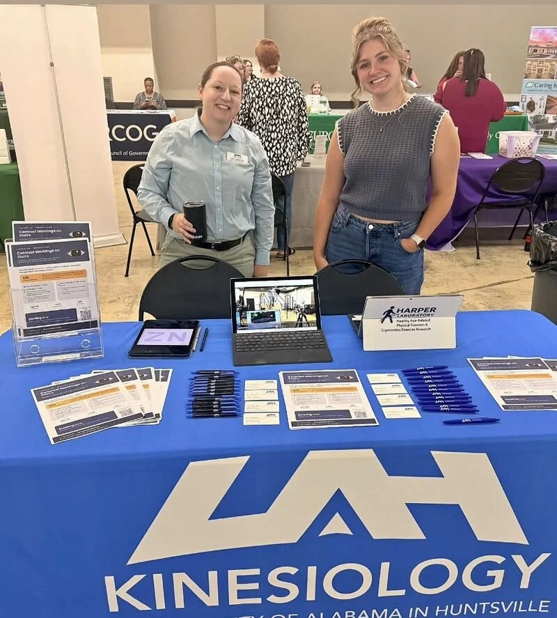 Two Harper Laboratory researchers at a UAH Kinesiology table at a community event, with flyers for the stair contrast markings study laid out in front of them.