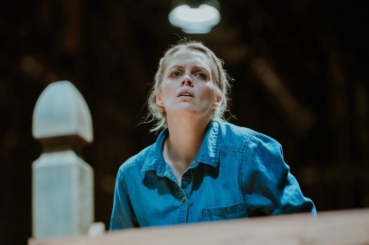 A person in a denim shirt looking upwards with a focused expression, indoor setting with dim lighting.