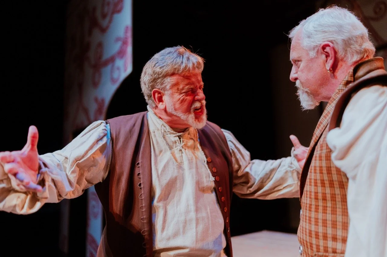 Two older men in historical clothing acting in an intense scene on stage.