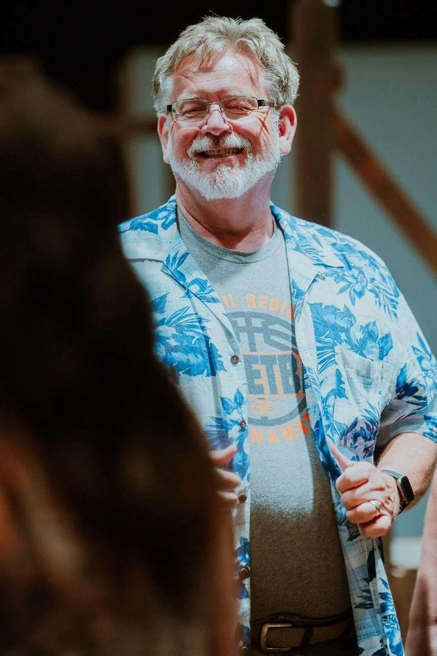 Smiling man with glasses wearing a blue floral shirt and a gray t-shirt at a casual event.