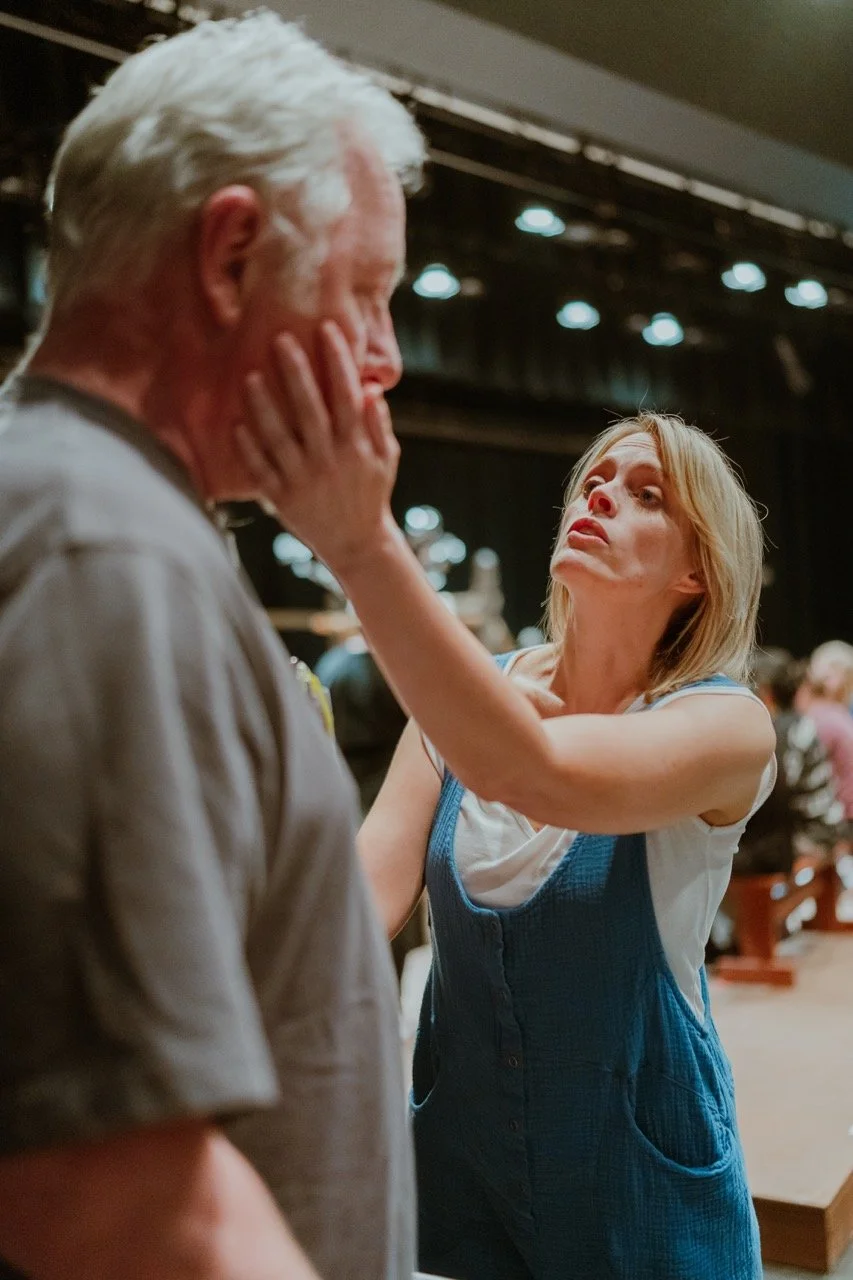 Two people interacting in a theater setting, with a woman putting her hand on a man's face.