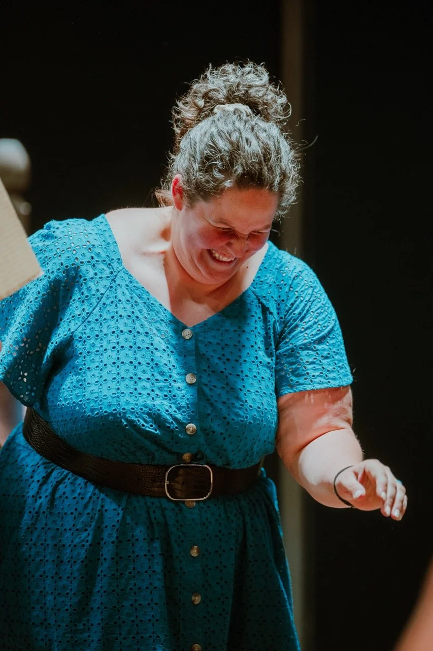 Woman smiling in blue dress with black belt, indoors.