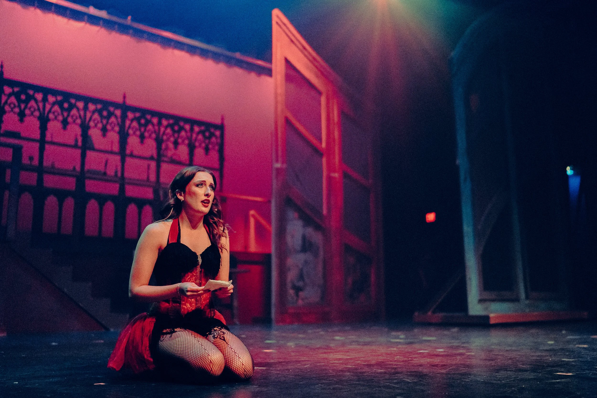 Woman in theatrical costume kneeling on stage with dramatic lighting