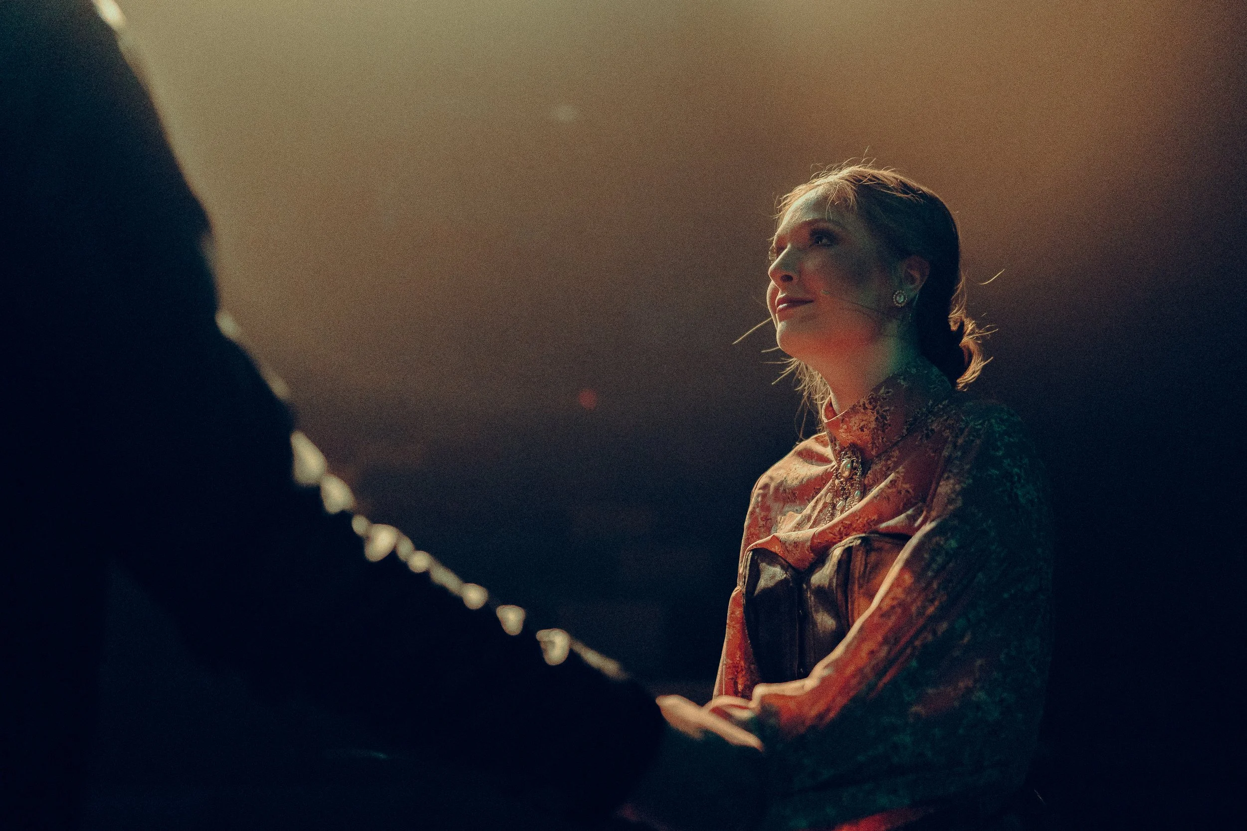 Person in dramatic lighting holding hand on stage or performance area.