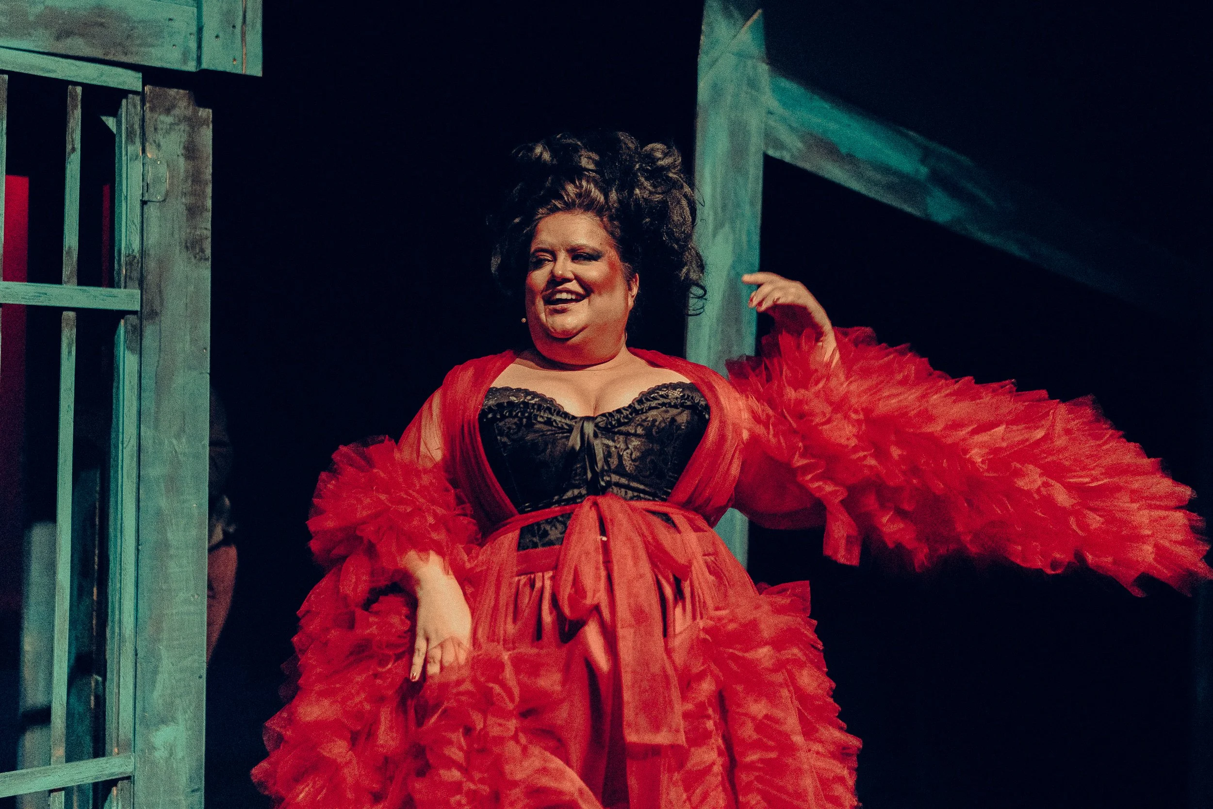 Person wearing a lace corset and red gown, performing on stage.