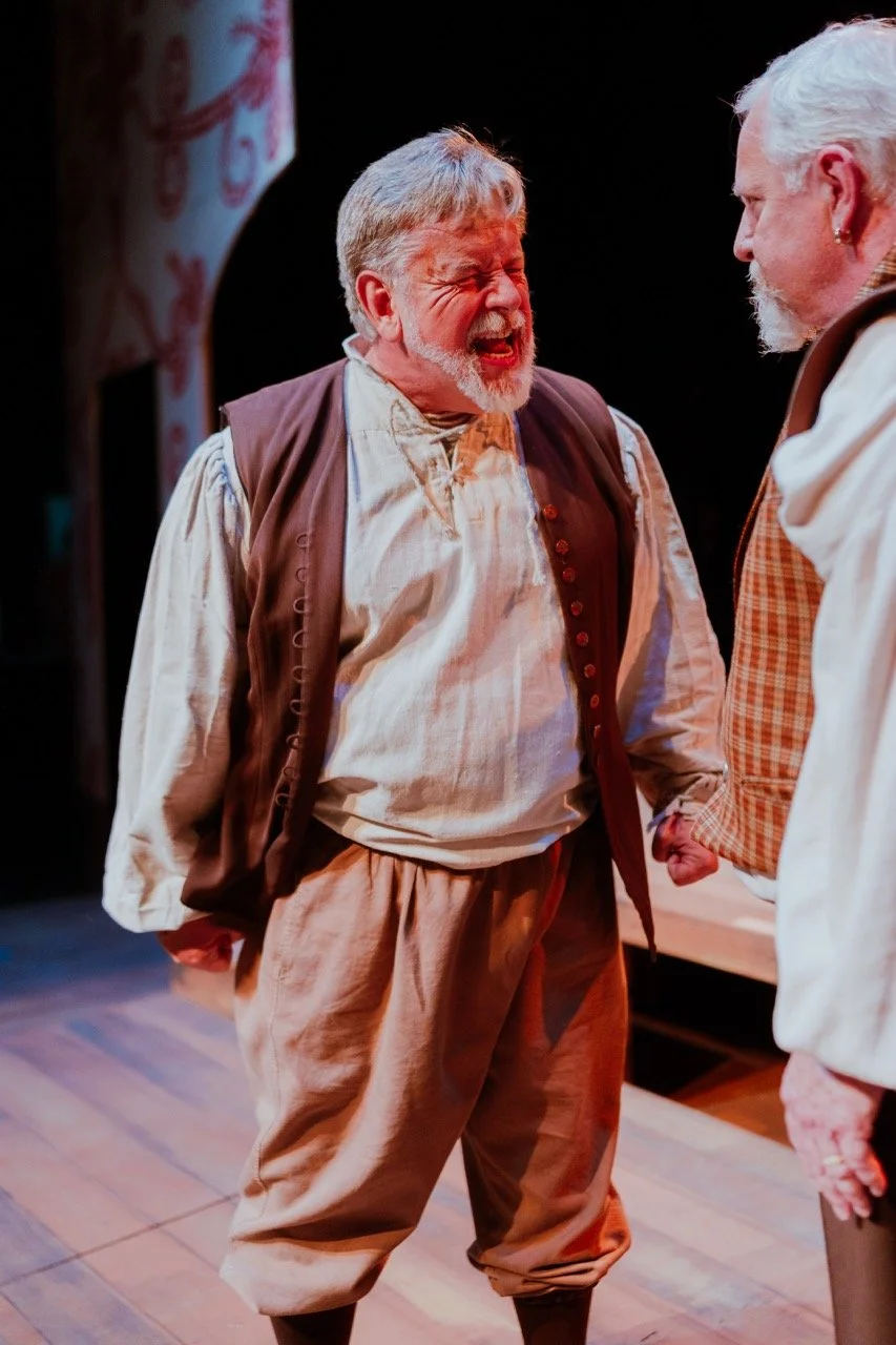 Two elderly men in period costumes perform passionately on stage.