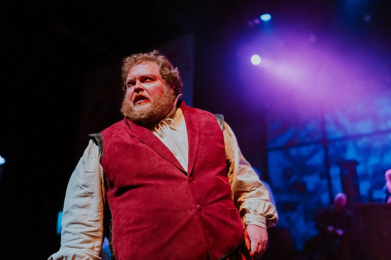 Man dressed in a period costume on stage with dramatic lighting.