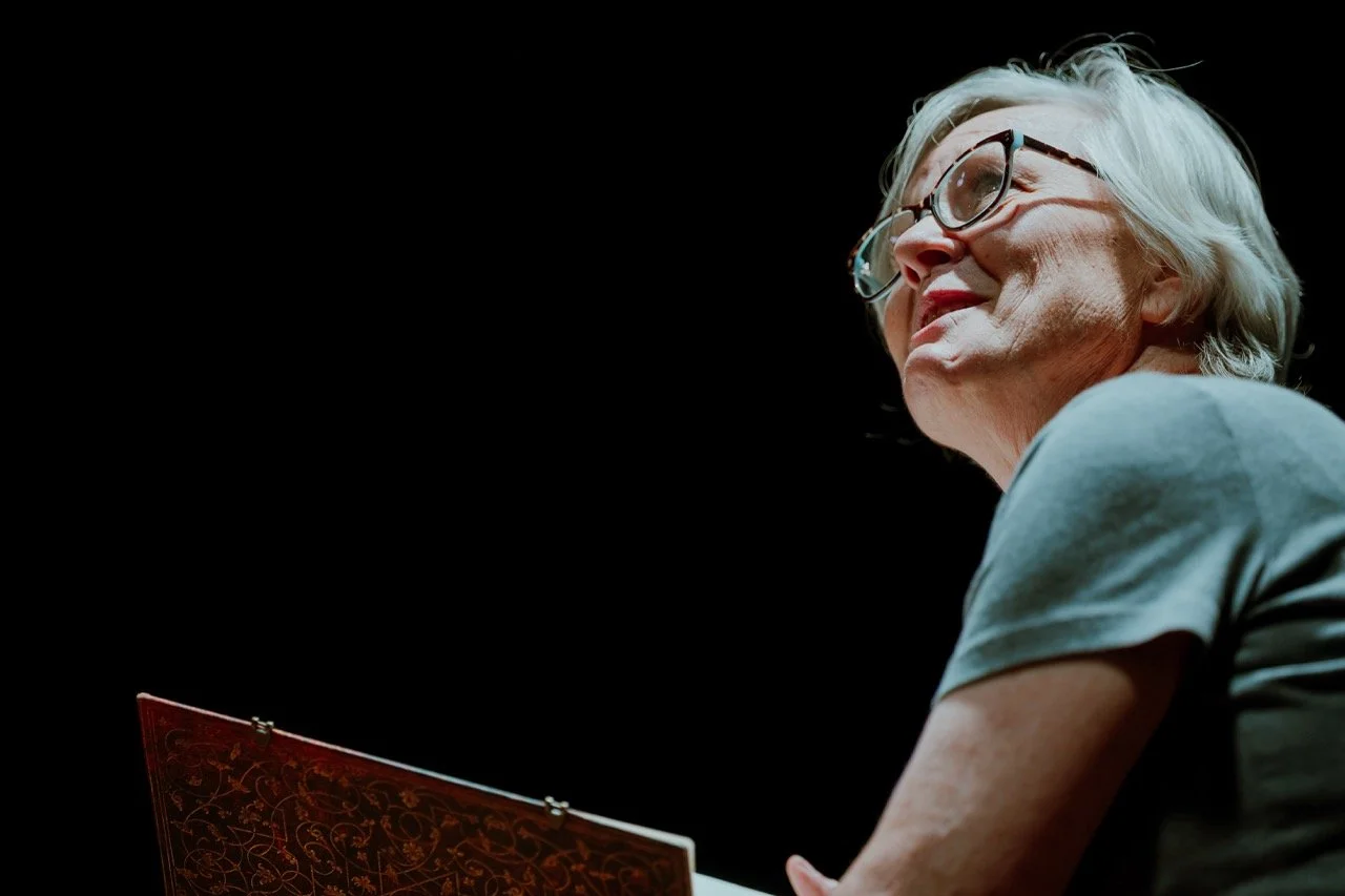Older woman with glasses reading a book, dark background.