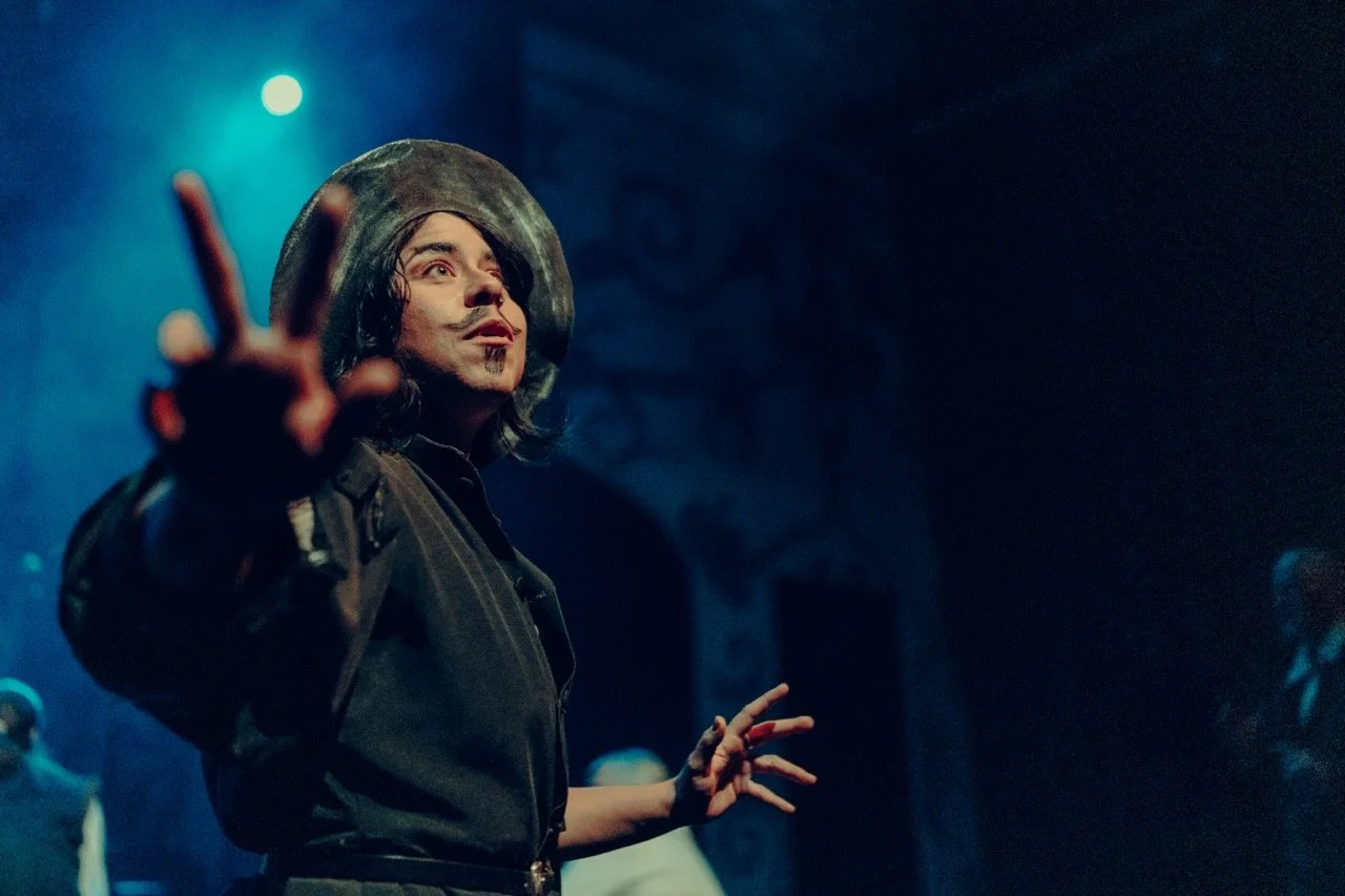 Theatrical performer in costume and makeup on stage with dramatic lighting.