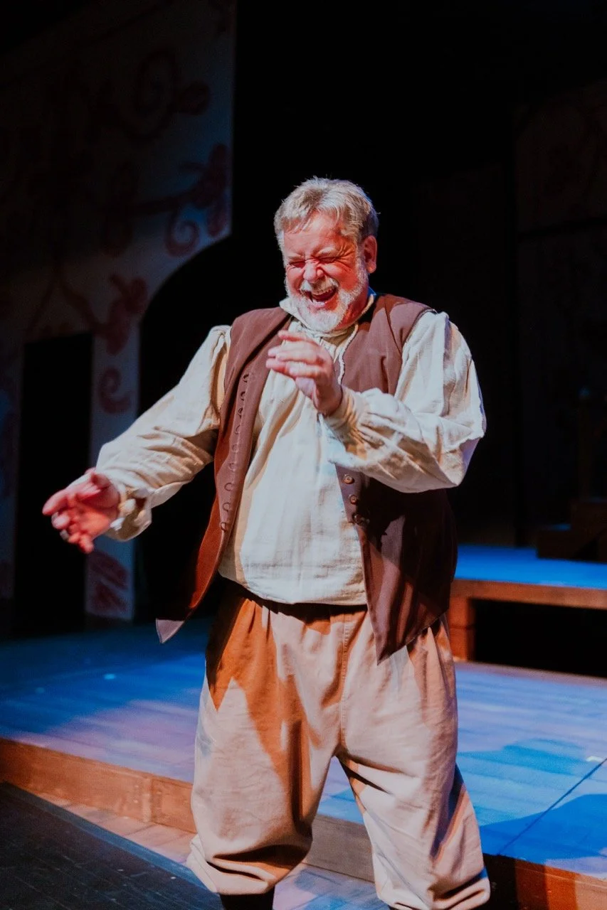 Actor on stage in period costume, laughing with eyes closed