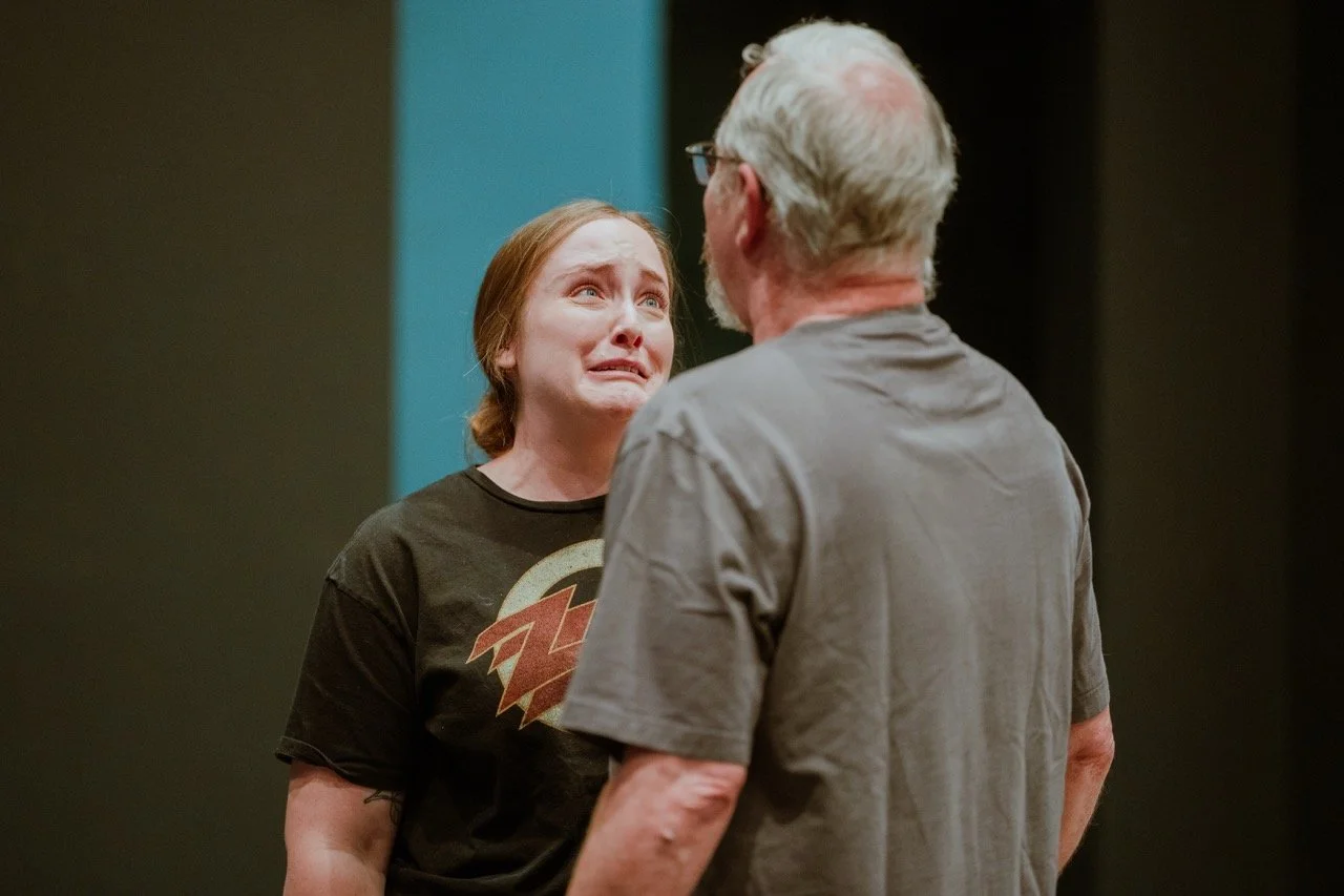 A woman with an emotional expression faces an older man indoors.