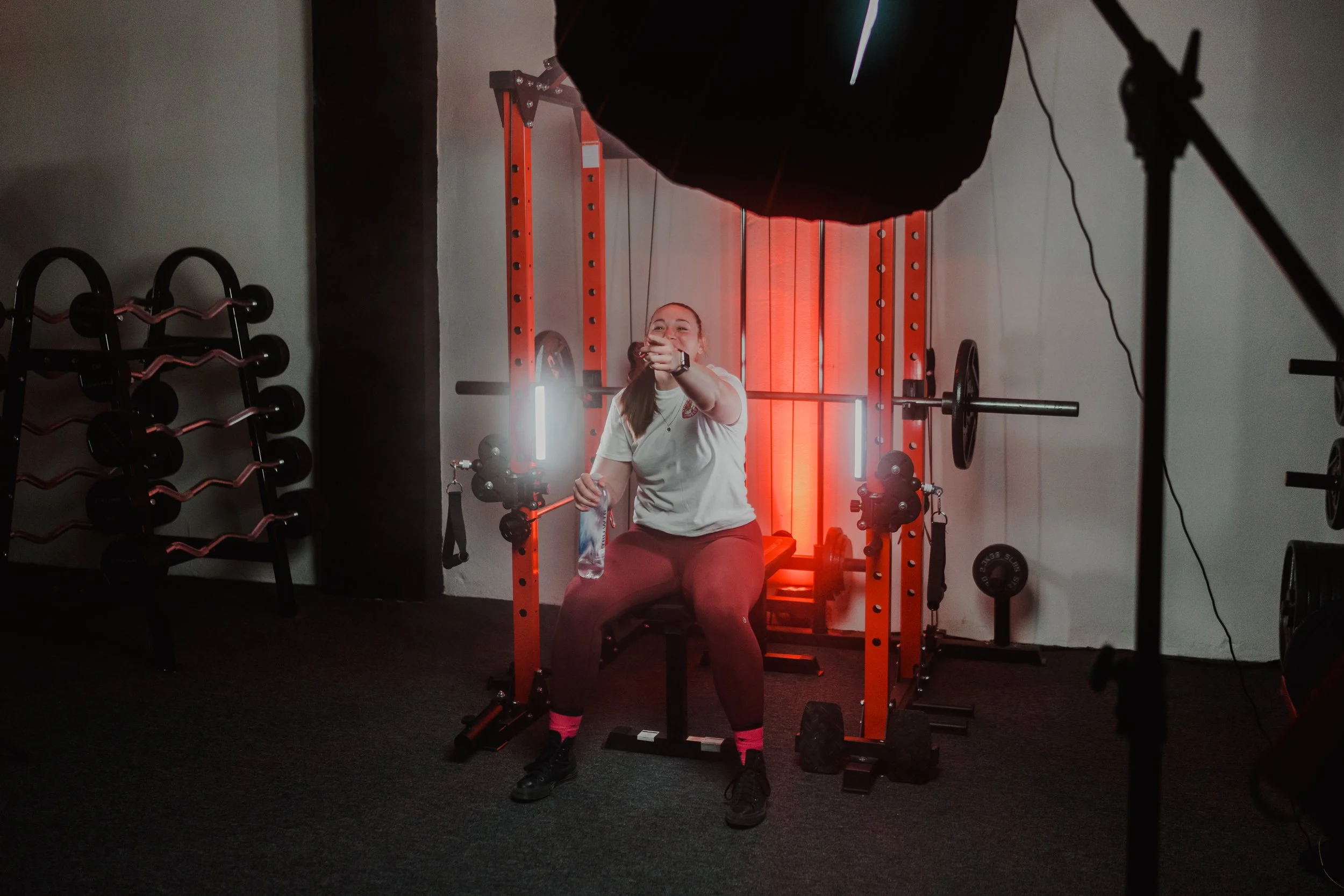 Person in gym sitting on weight bench holding a water bottle, with a barbell rack and weights in the background.
