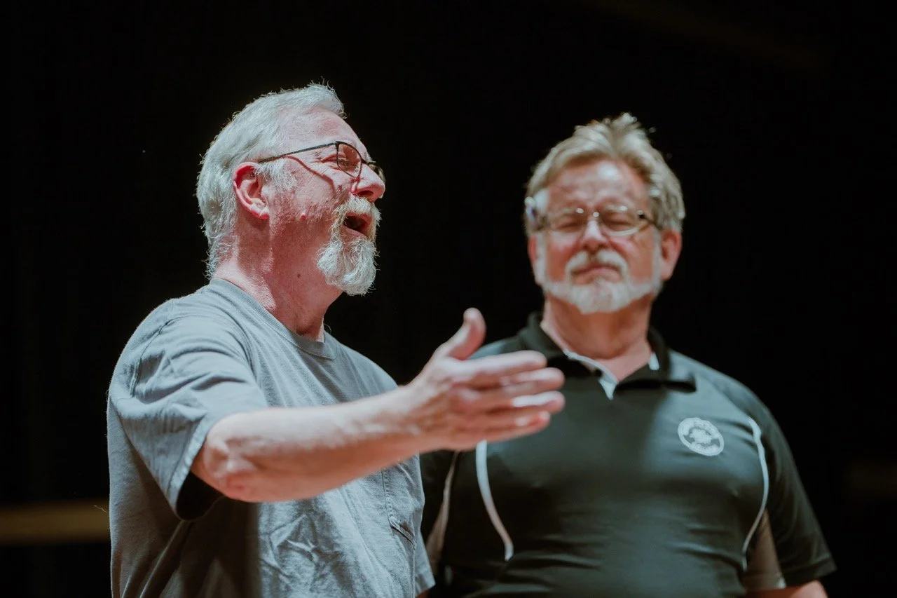 Two men performing on stage, one speaking passionately with gestures.