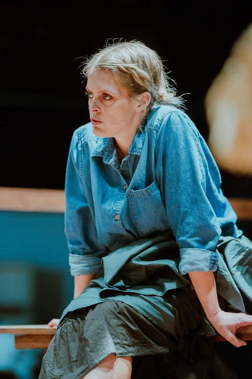 Person in a blue denim shirt sitting on a wooden bench, looking thoughtful.
