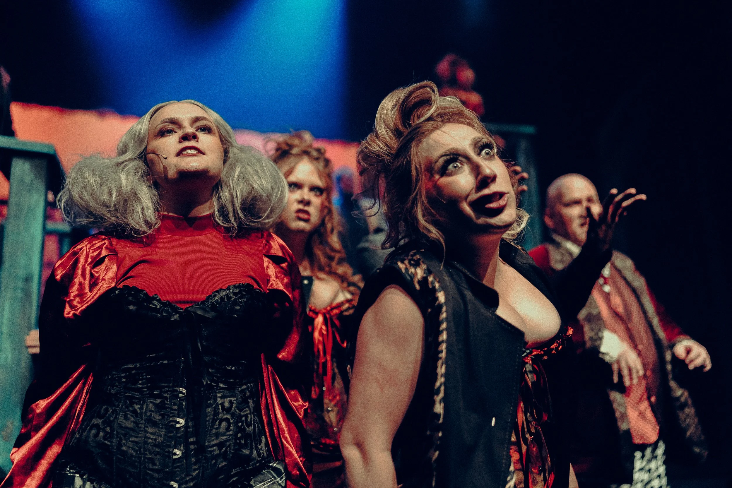 Performers in theatrical costumes during a dramatic stage performance, featuring vibrant lighting and expressive facial expressions.
