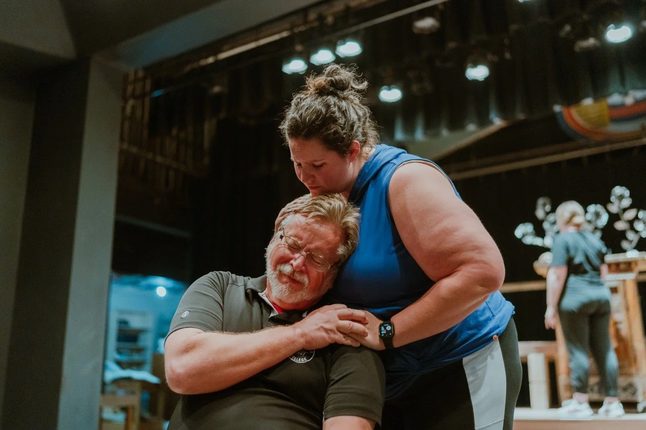 An emotional moment between a man and woman on a stage, the woman comforting the man.