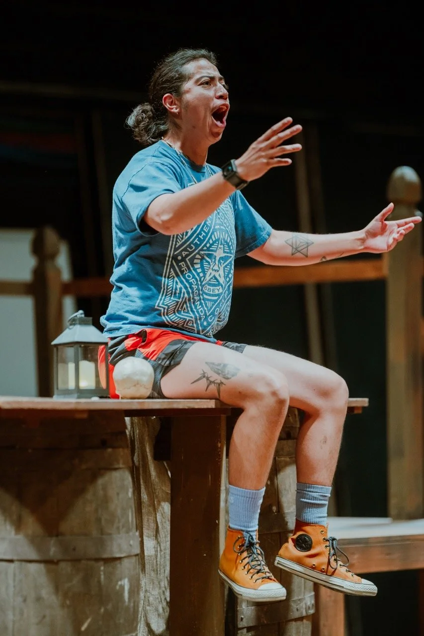 Person sitting on a wooden platform with outstretched arms, wearing a blue T-shirt and orange high-top sneakers.