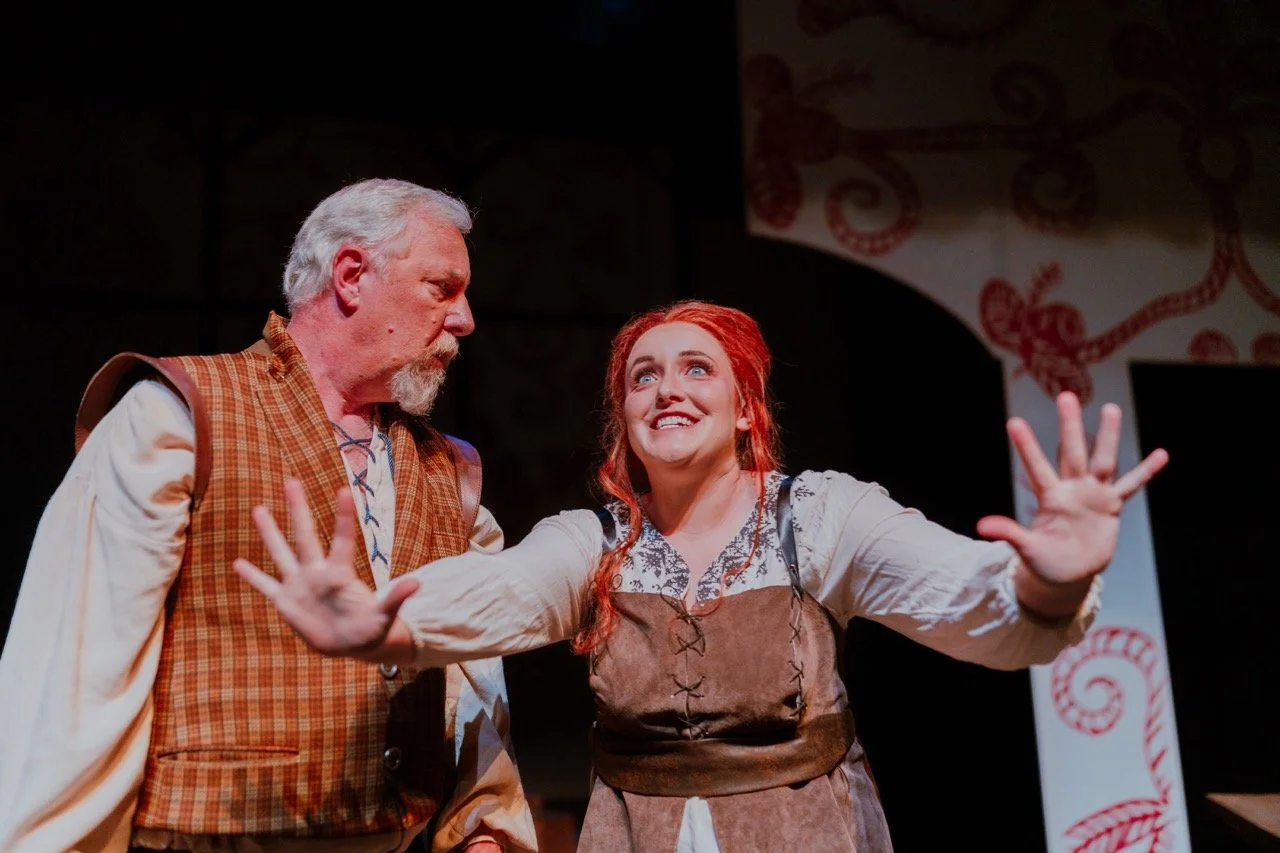 Theatrical performance with two actors in period costumes, one gesturing passionately.
